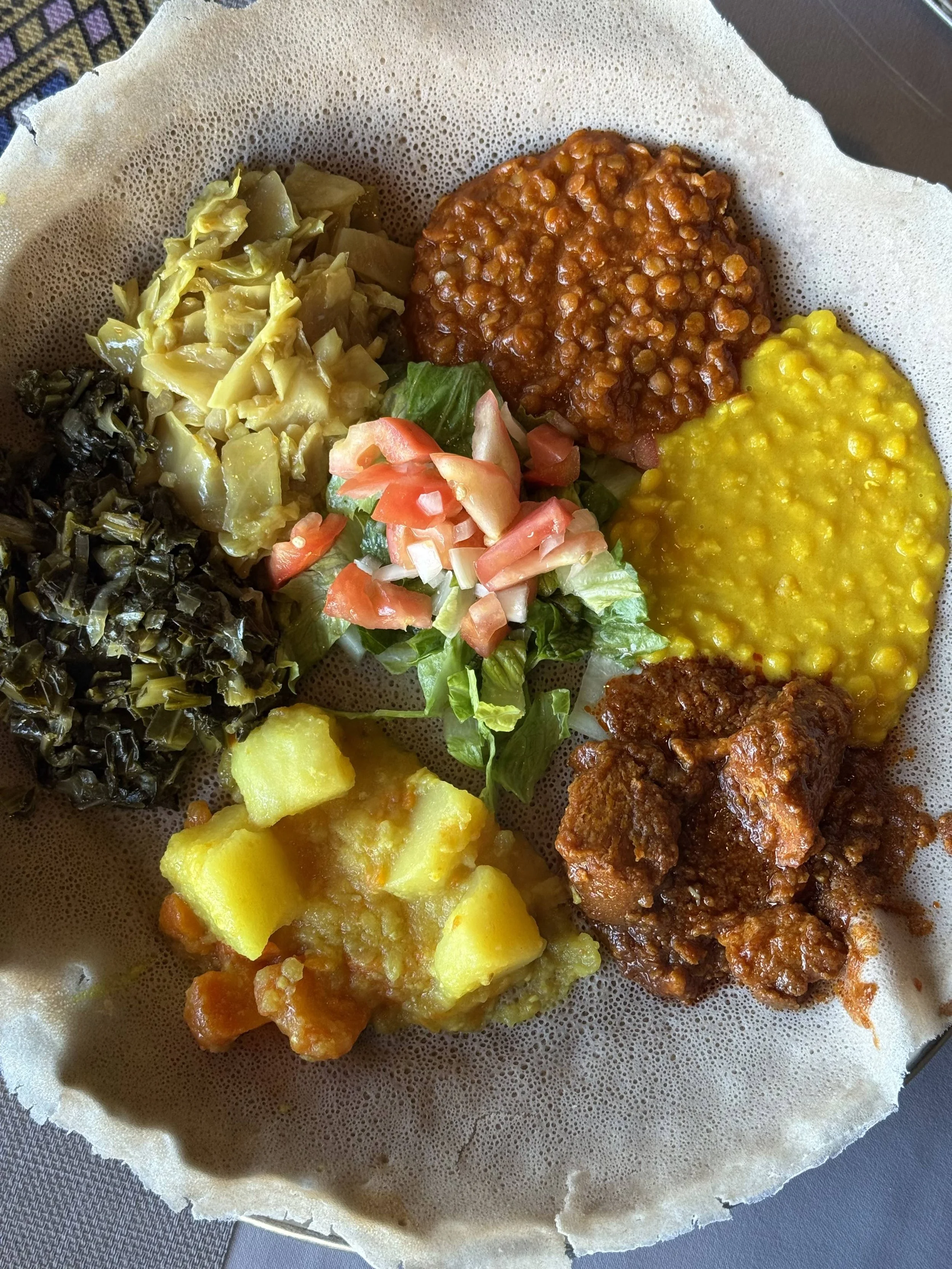 Plate of traditional Ethiopian Injera bread topped with various vegetarian stews and vegetables, including lentils, split peas, and cooked greens.