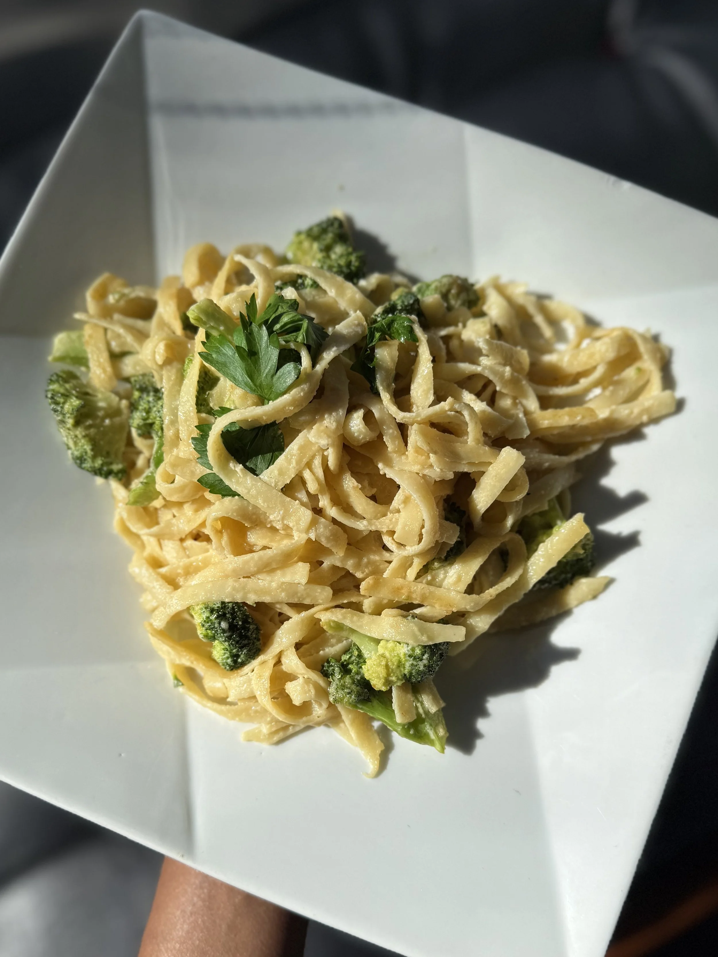 A plate of fettuccine pasta with broccoli and parsley garnished on a square white dish.