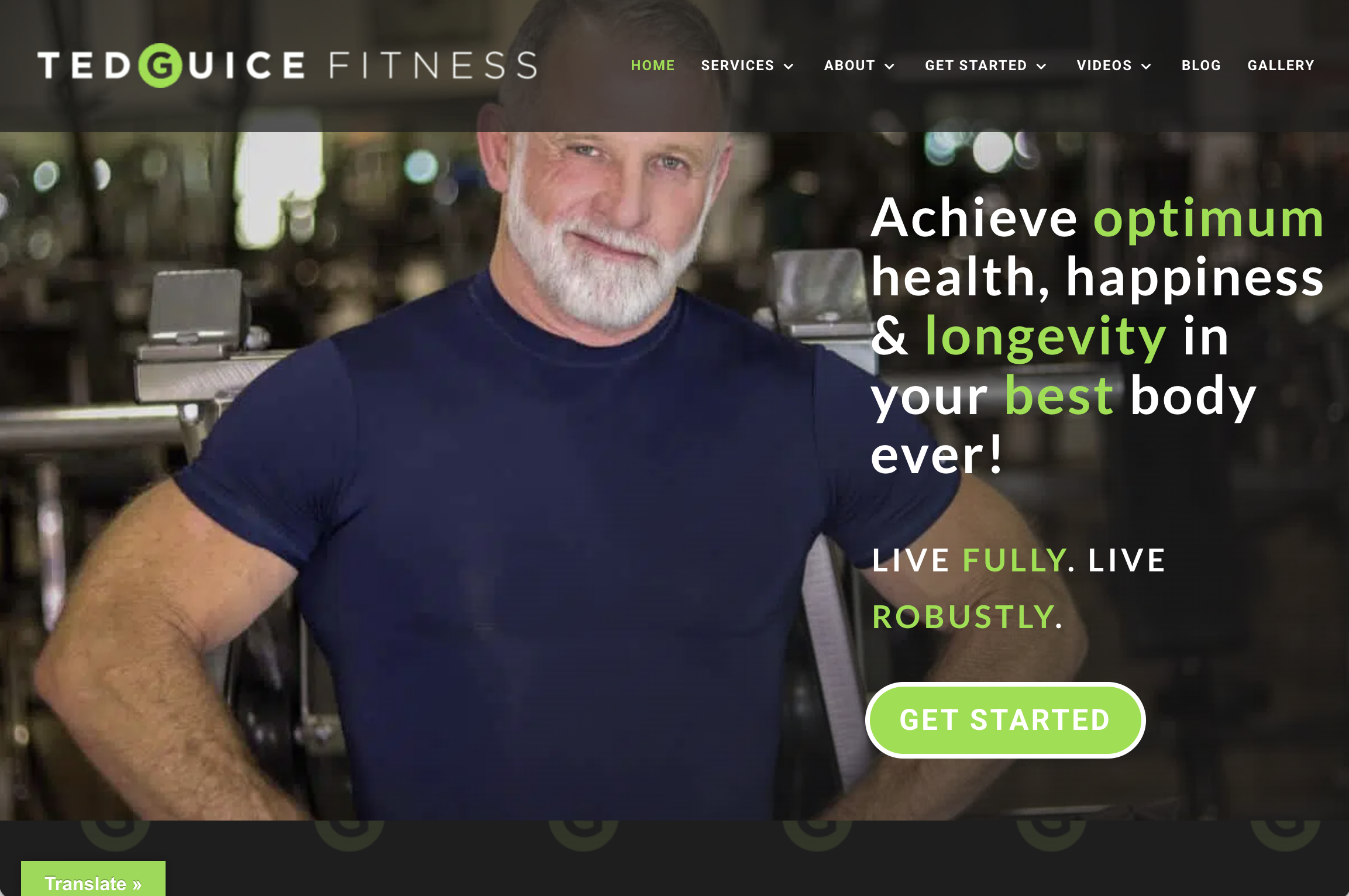 A smiling man with a white beard and short hair wearing a navy blue t-shirt in a gym or fitness center.