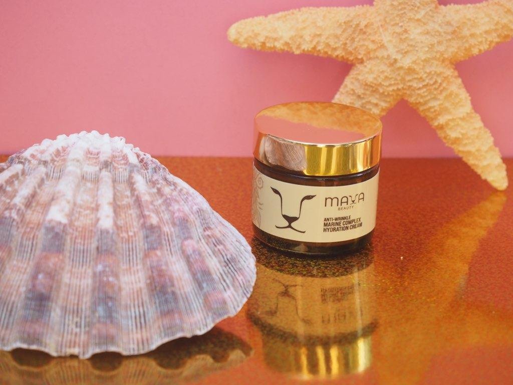A jar of Maya Beauty Anti-Wrinkle Marine Complex Hydration Cream, a white seashell, and a starfish on a pink background with a reflective surface.