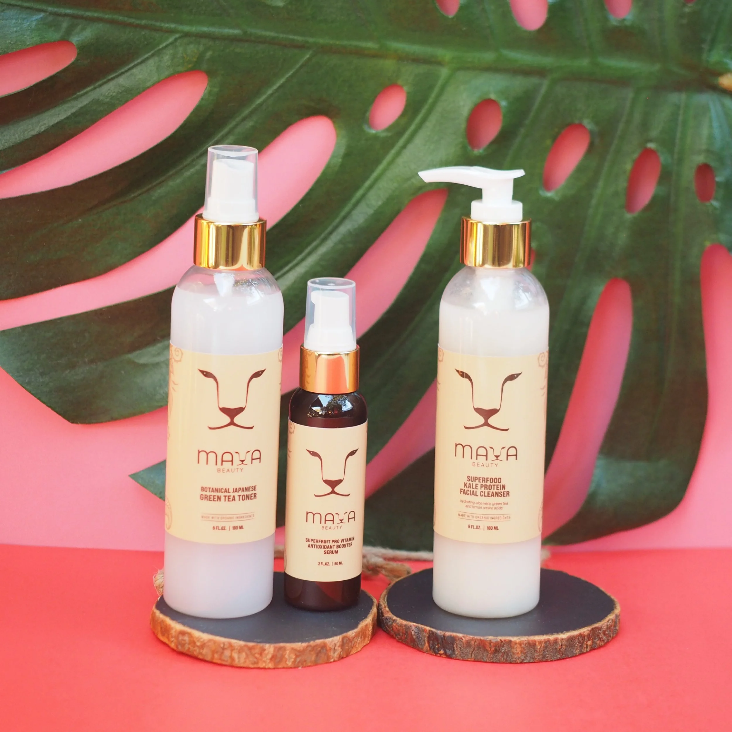 Three skincare product bottles on wooden coasters against a pink background with a large green monstera leaf with pink holes.