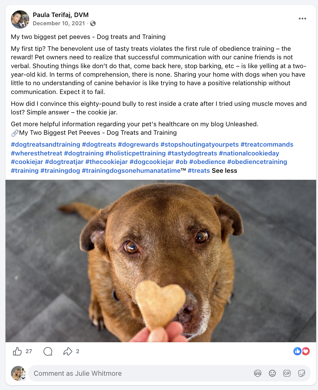 A brown dog looking up at the camera while holding a heart-shaped dog treat on its nose.