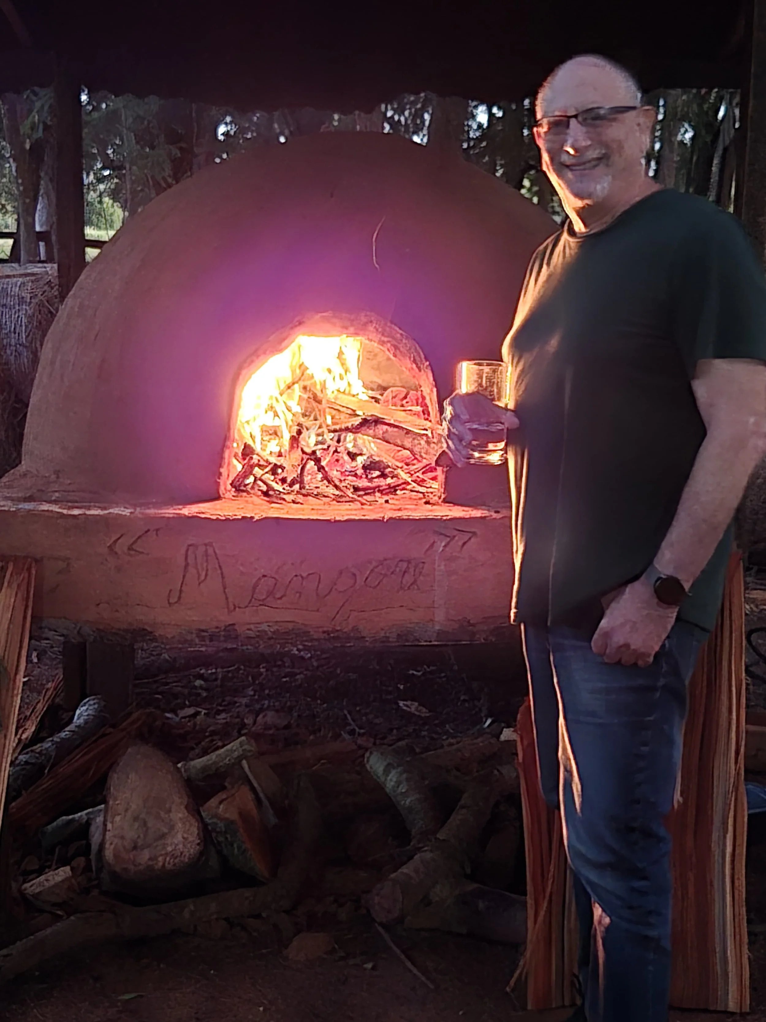 Mark Wodika standing in front of a wood-fired traditional outdoor oven - a Tatakua.