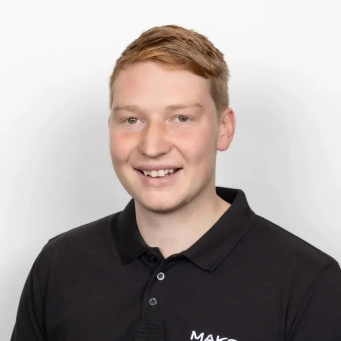 A young man with ginger hair wearing a black polo shirt smiling against a plain white background.