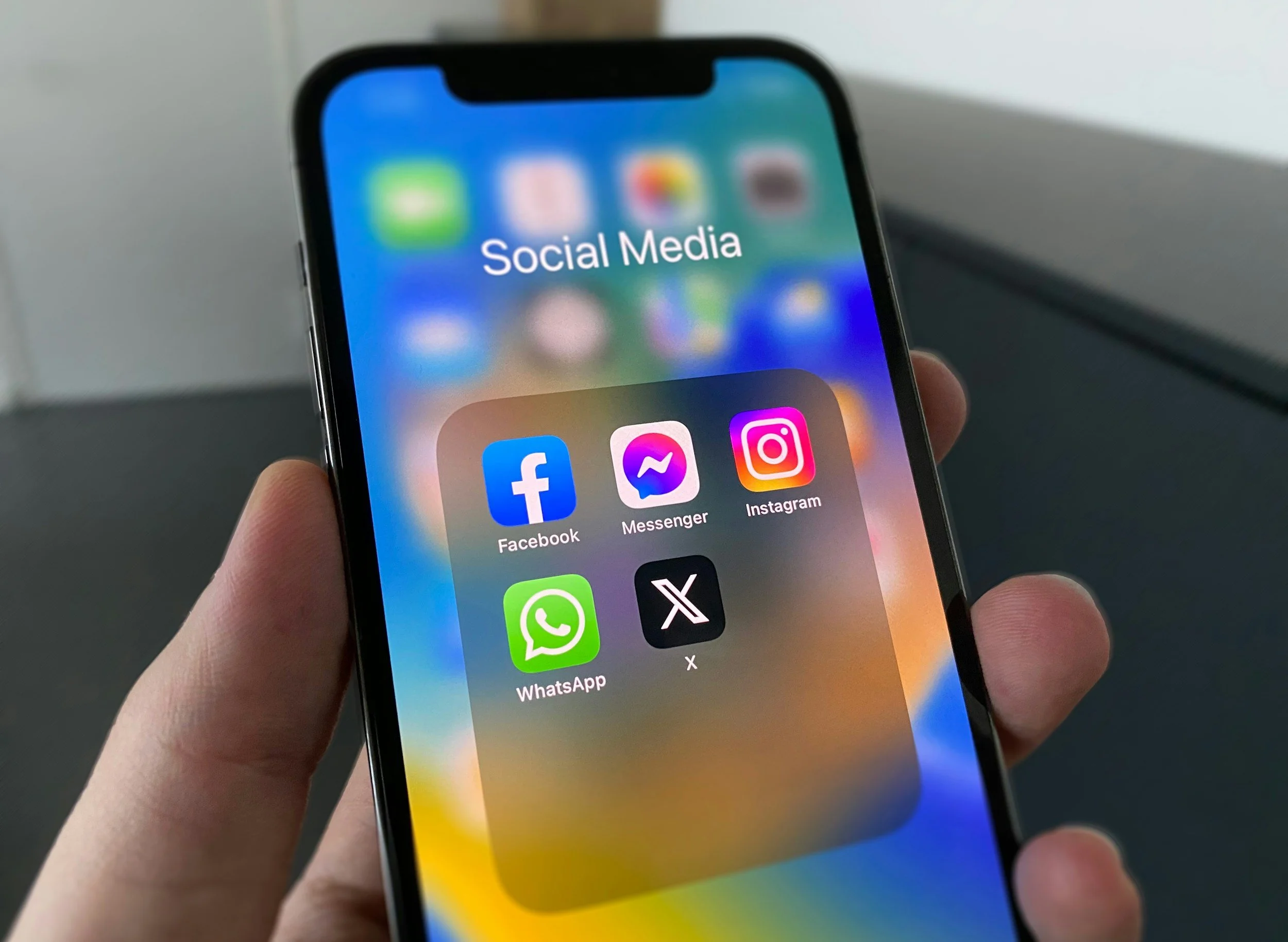 Close-up of a smartphone screen displaying social media apps including Facebook, Messenger, Instagram, WhatsApp, and X in a person's hand.