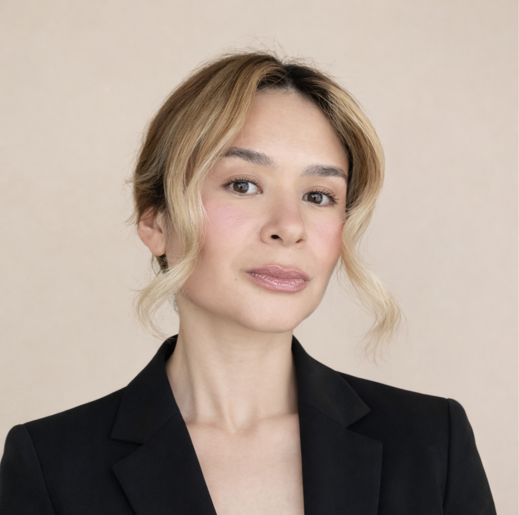 A woman with wavy blonde hair wearing a black blazer against a light background.