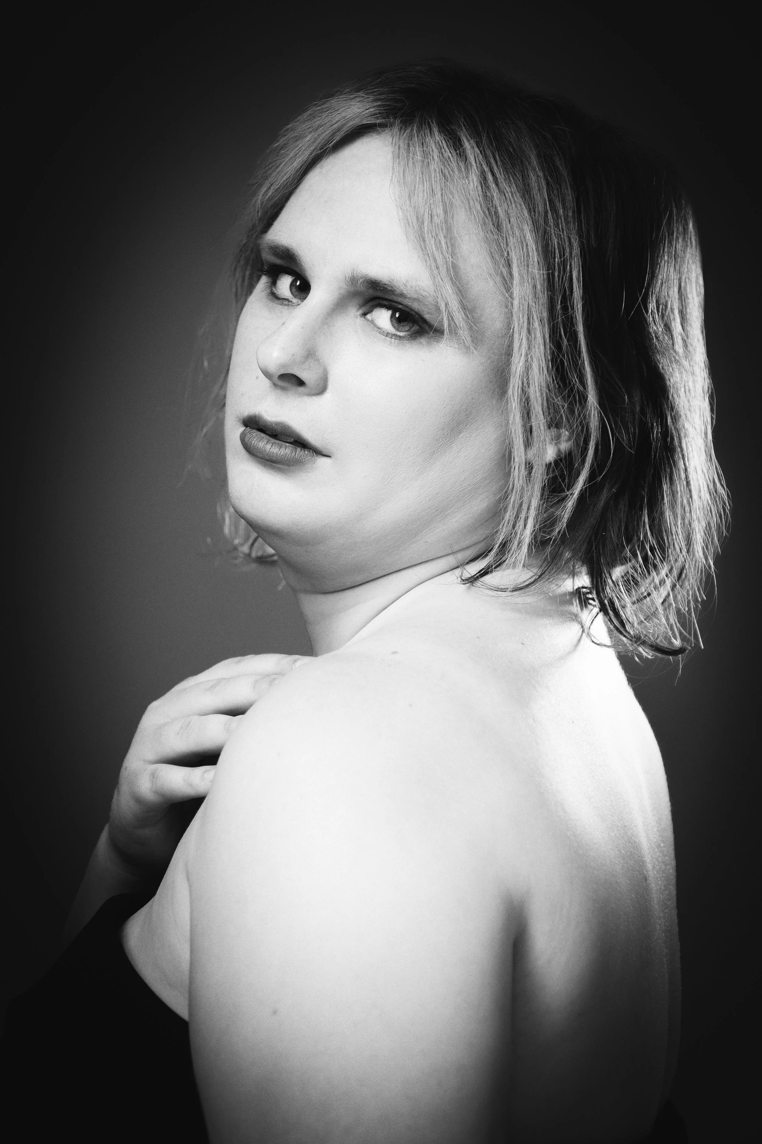 Black and white portrait of a woman with short hair, looking at the camera, with one shoulder exposed and her hand resting on her shoulder.