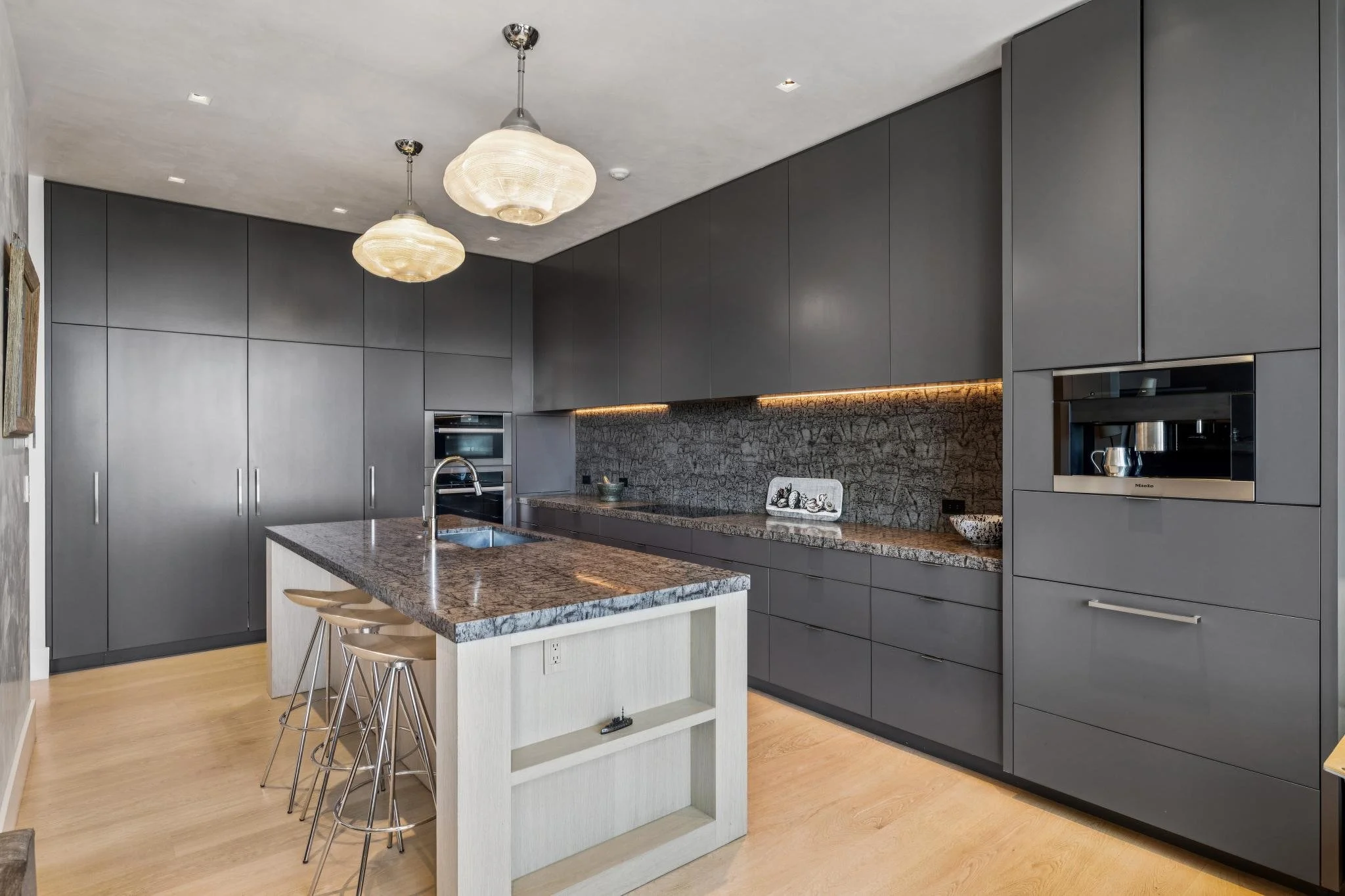 Modern kitchen with gray cabinets, marble countertop on kitchen island, and pendant lighting.