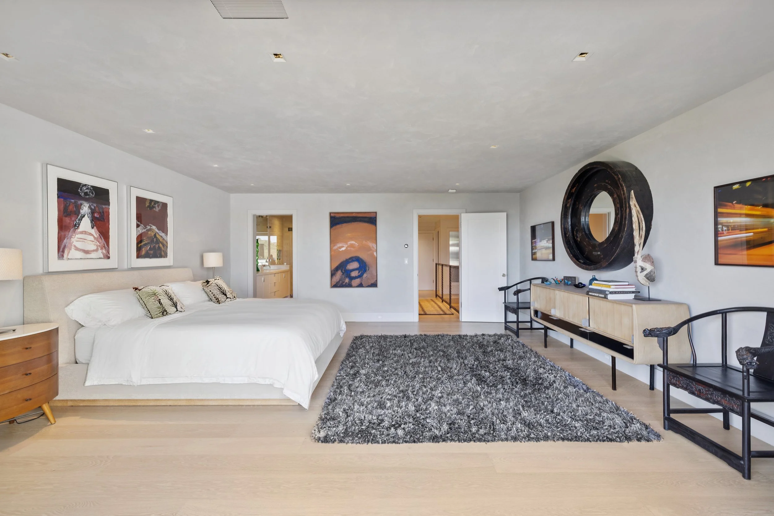 A bedroom with a large bed, artwork on the walls, a textured gray rug, and modern decor.