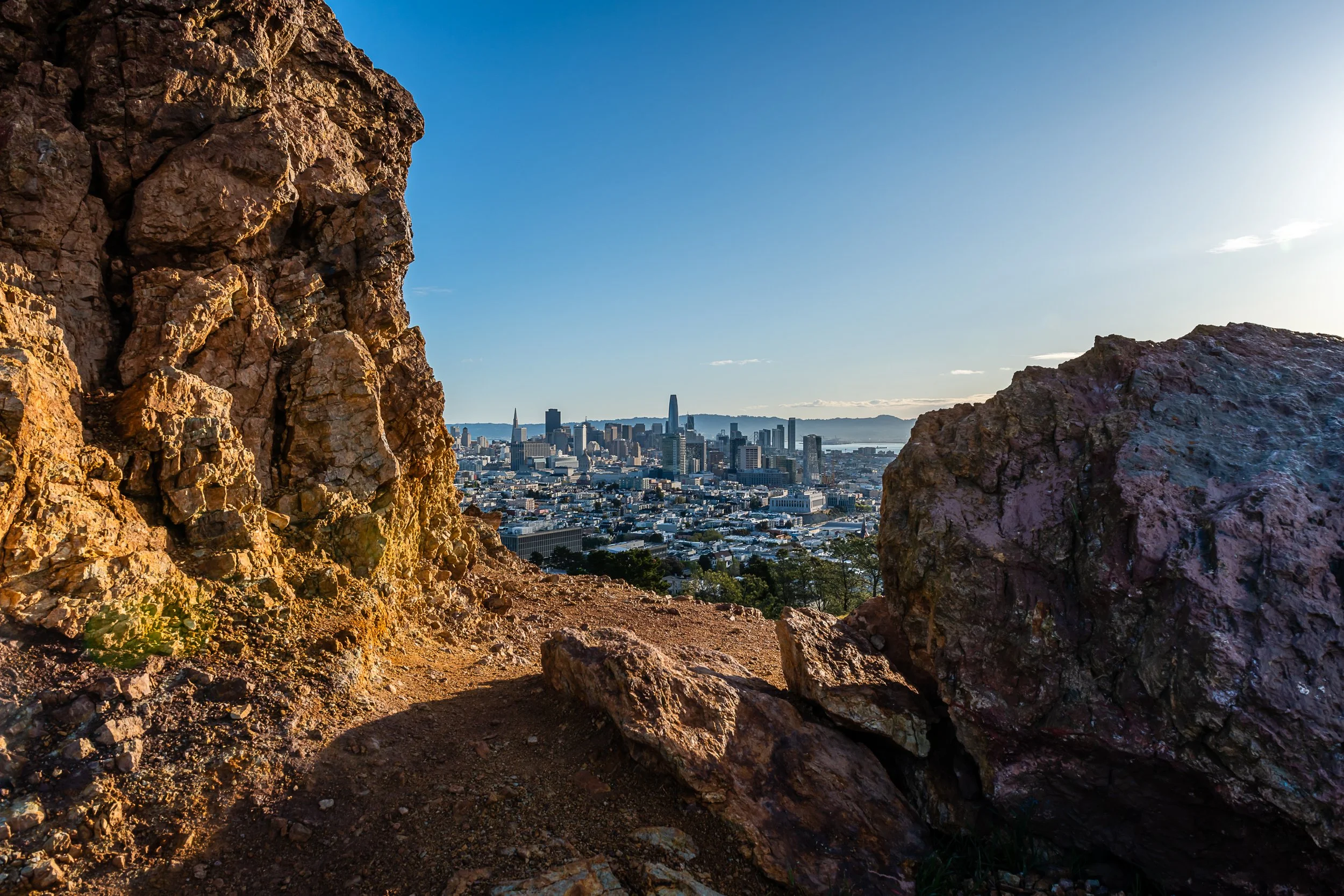View of a city skyline through a gap between large rocks with clear sky in the background.