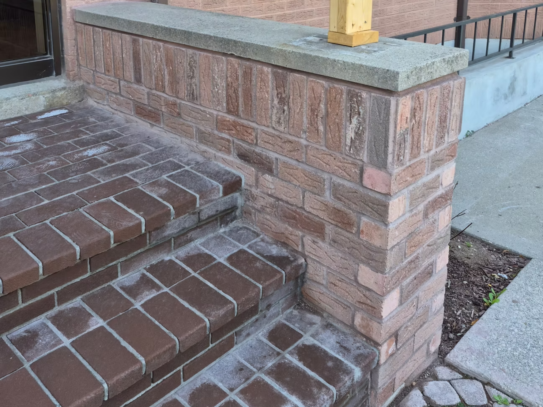 Close-up of brick stairs and a brick wall with concrete and wood railing on a porch.
