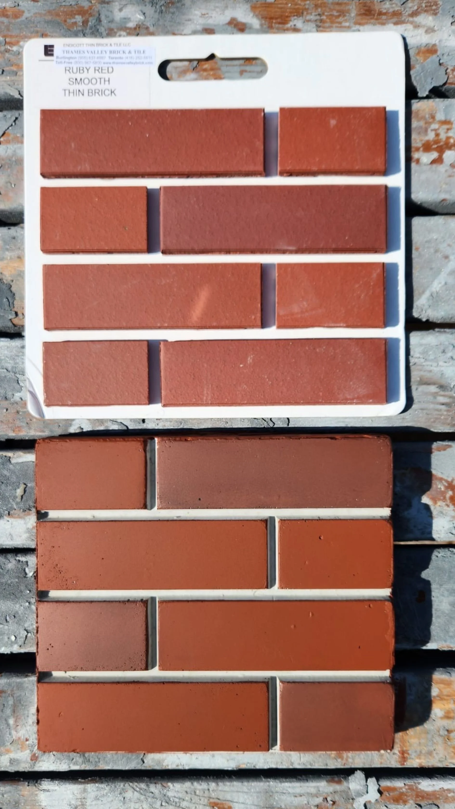 Tile sample board displaying various shades of red and orange bricks, labeled from Ruby Red to darker shades, arranged in rows on a white display board outdoors.