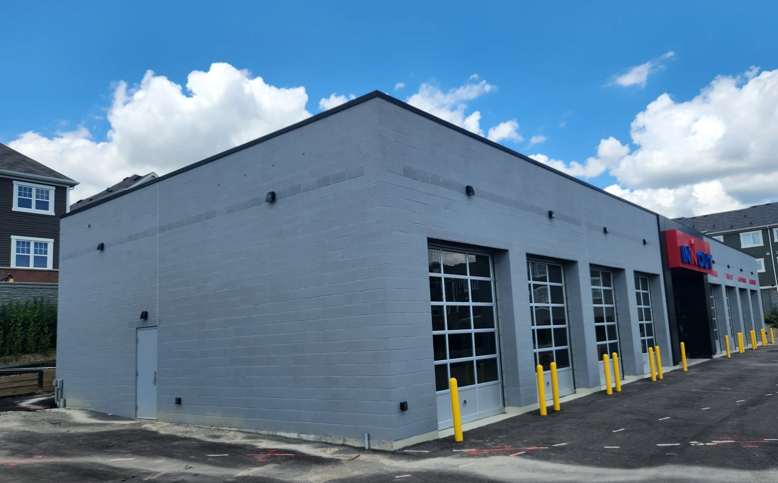 A modern commercial building with a light gray brick exterior, large windows, and a sign that reads "INNOT" on a bright, partly cloudy day.
