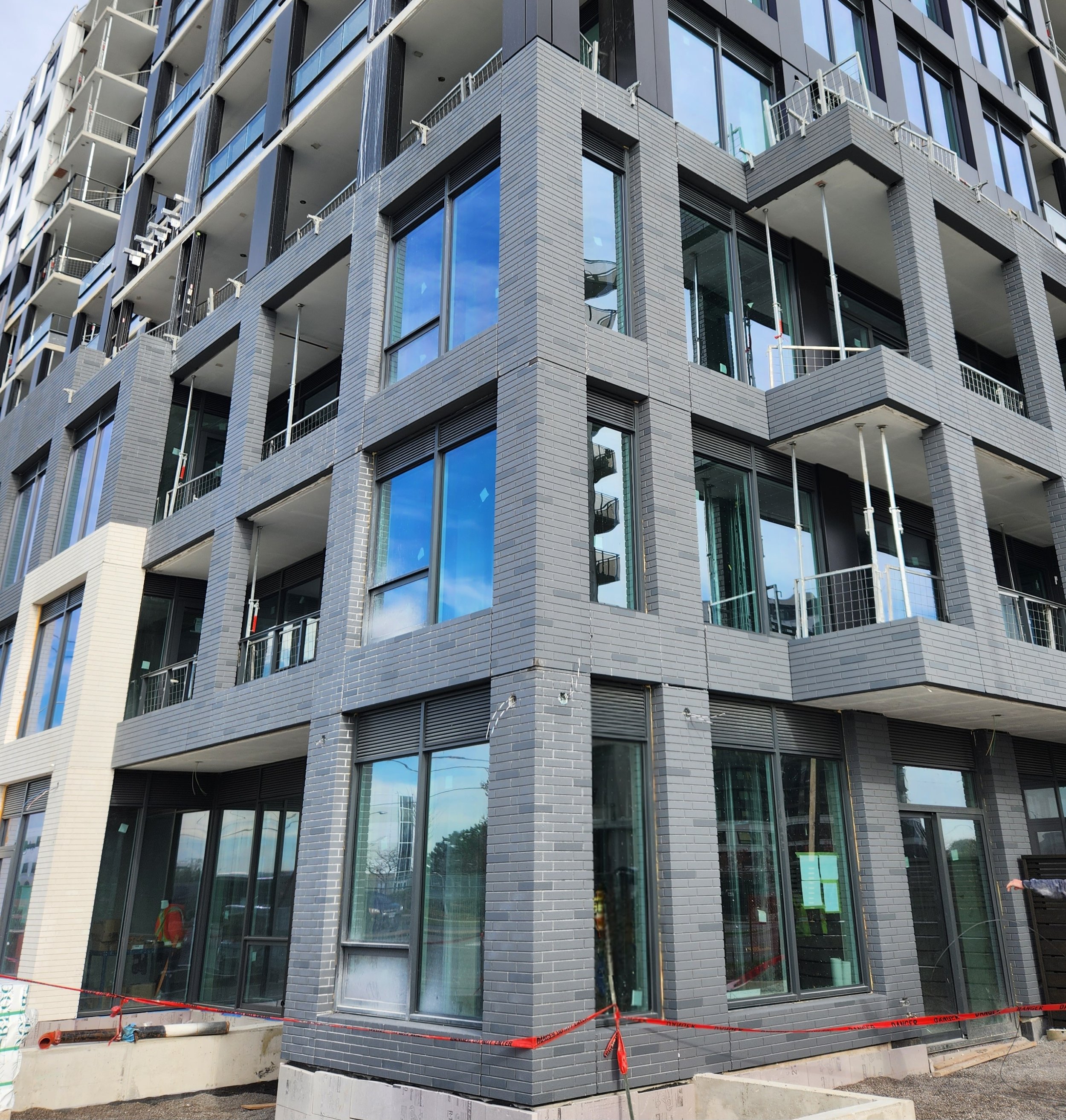 A modern multi-story building under construction with black brick exterior, large glass windows, and small balconies. Construction materials and safety barriers are visible at the ground level.