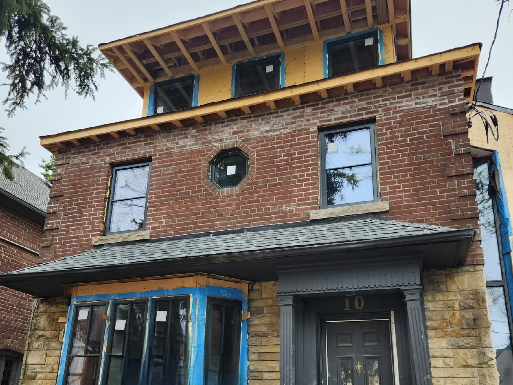 Front view of a house under renovation, with a brick exterior, new window frames, and construction materials around.