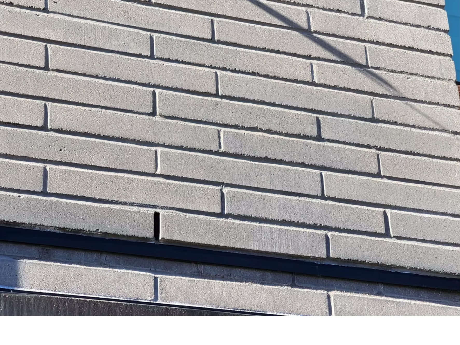 Close-up view of a white brick wall with visible horizontal mortar lines, casting slight shadow.