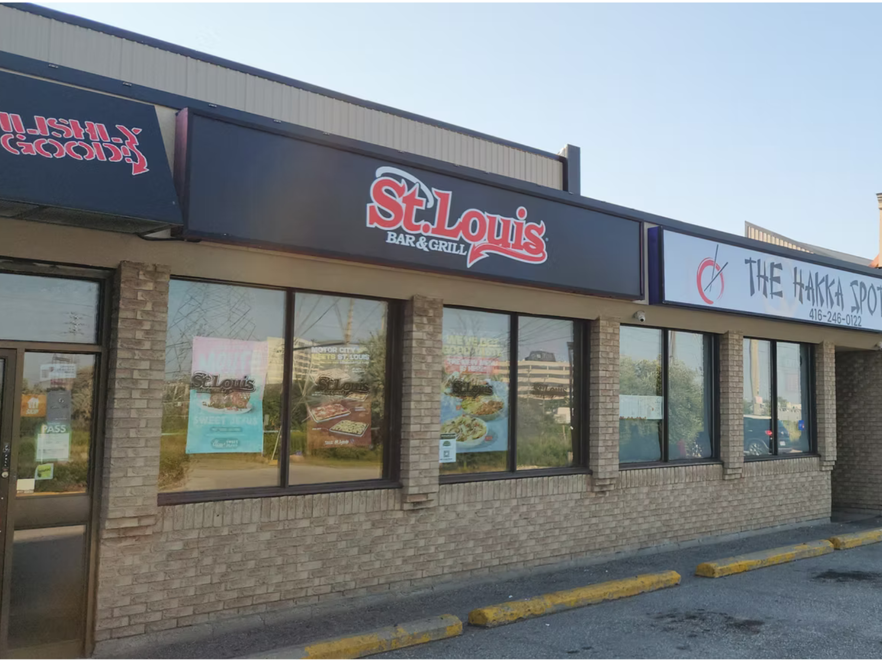 Exterior of a restaurant with a brick facade and large windows, featuring signs for St. Louis Bar & Grill and The Hakka Spot.