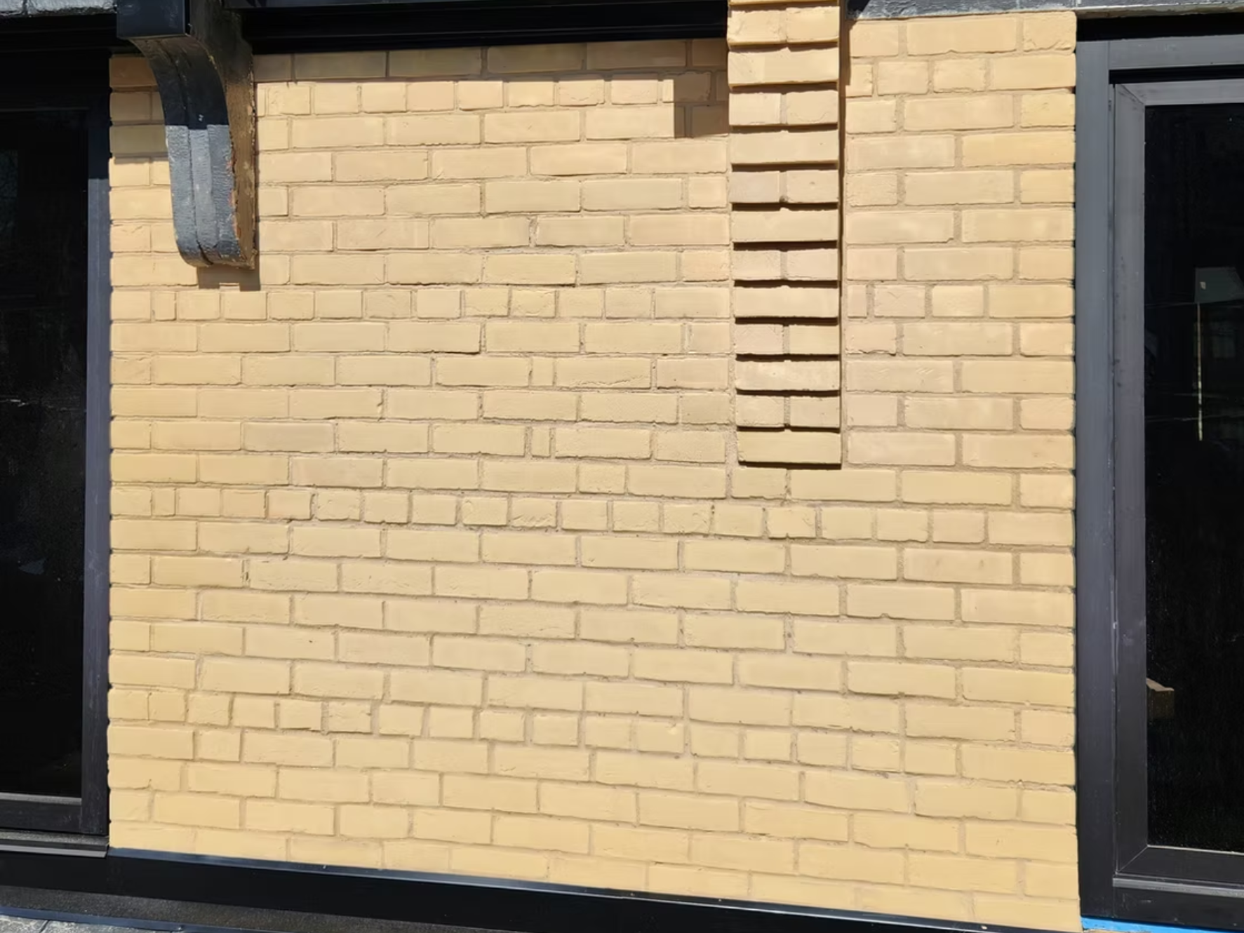 Yellow brick wall with a black window frame on the right and a black structure on the left