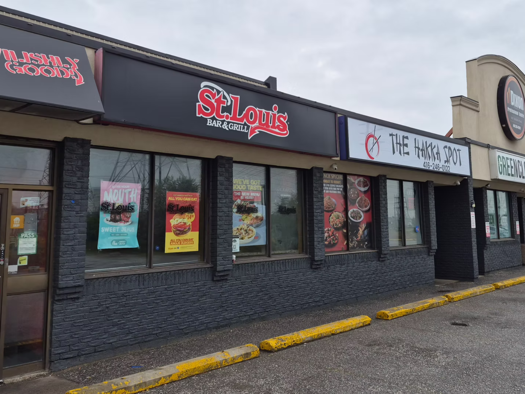 Signage indicating the presence of a bar and grill named St. Louis, and a restaurant called The Hakka Spot, in a strip mall with large front windows and black brick exterior. Yellow parking lot curbs are visible at the bottom.