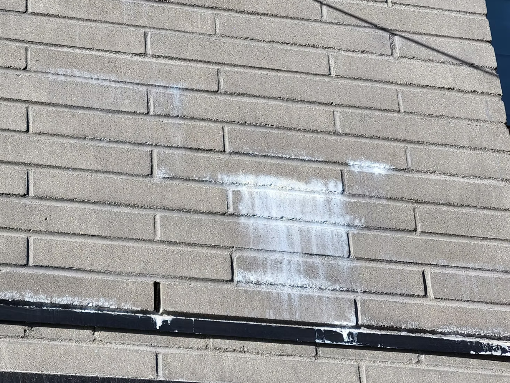 A brick wall with some white paint streaks and streaks on the black base that runs along the bottom of the wall.