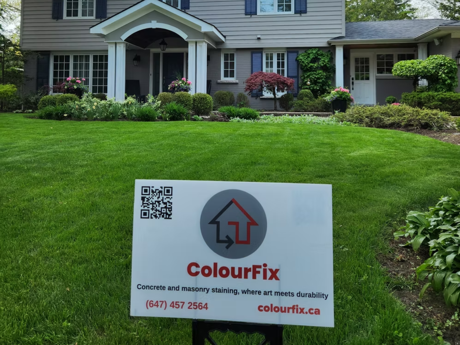 A house with a well-maintained green lawn and landscaped garden. A sign in front of the lawn reads "ColourFix" and advertises concrete and masonry staining services, with a QR code, phone number, and website.