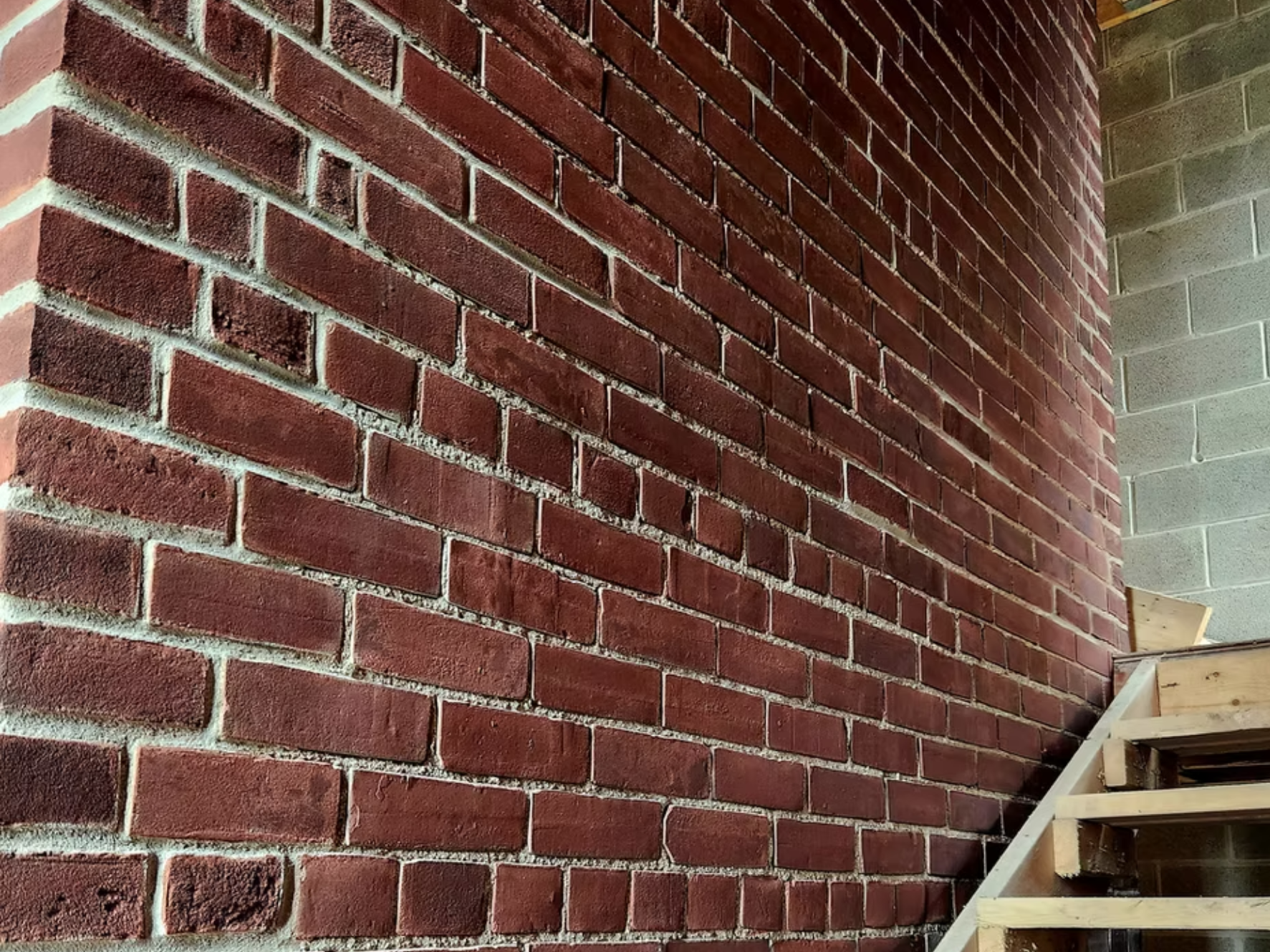 Red brick wall at a construction site with a wooden staircase to the right.