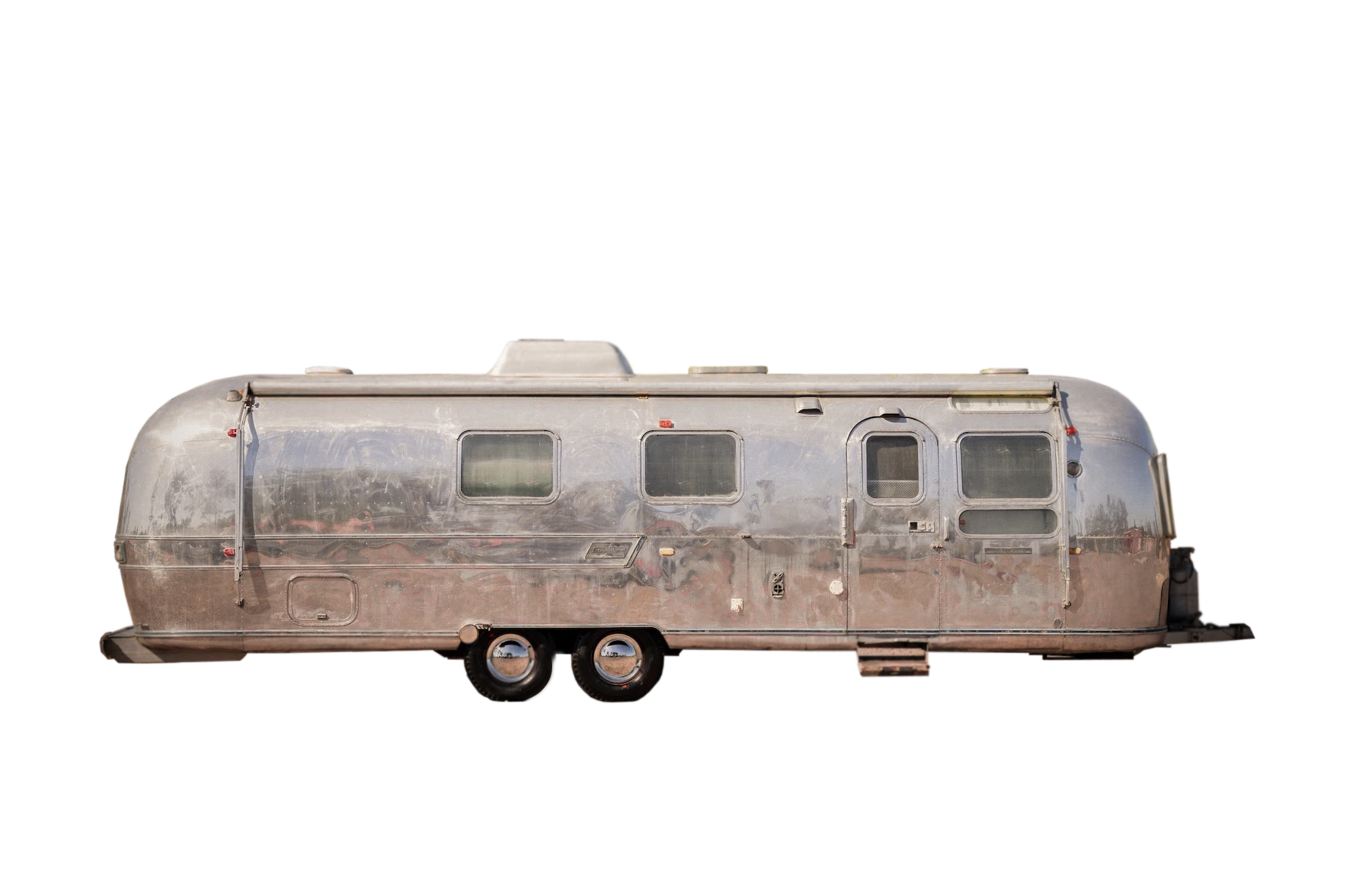 A vintage silver travel trailer with four windows, two axles, and rounded edges, isolated on a black background.