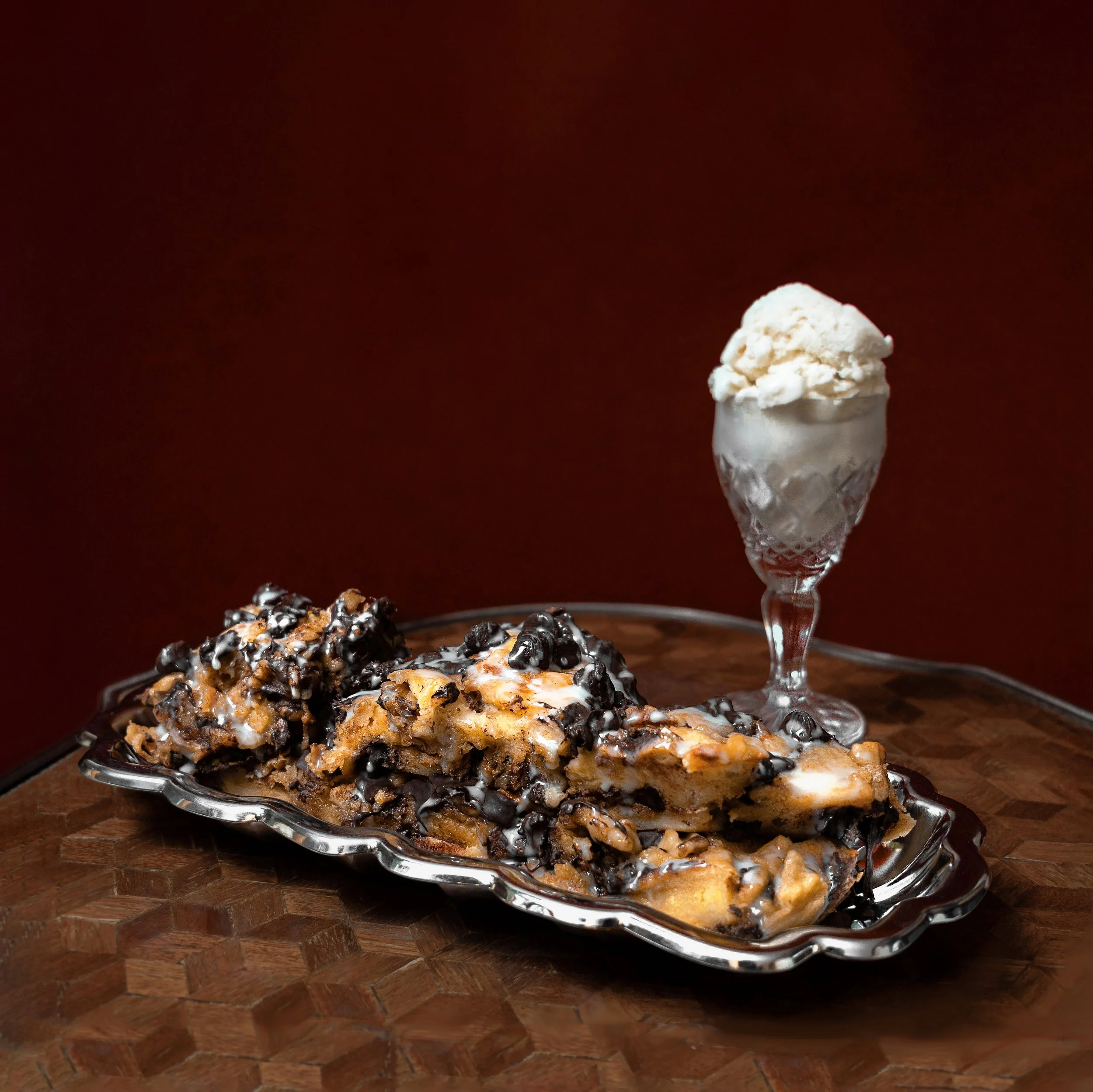 Ice cream in a glass with chocolate chips and a cookie pie with chocolate chips on a glass plate on a wooden table.