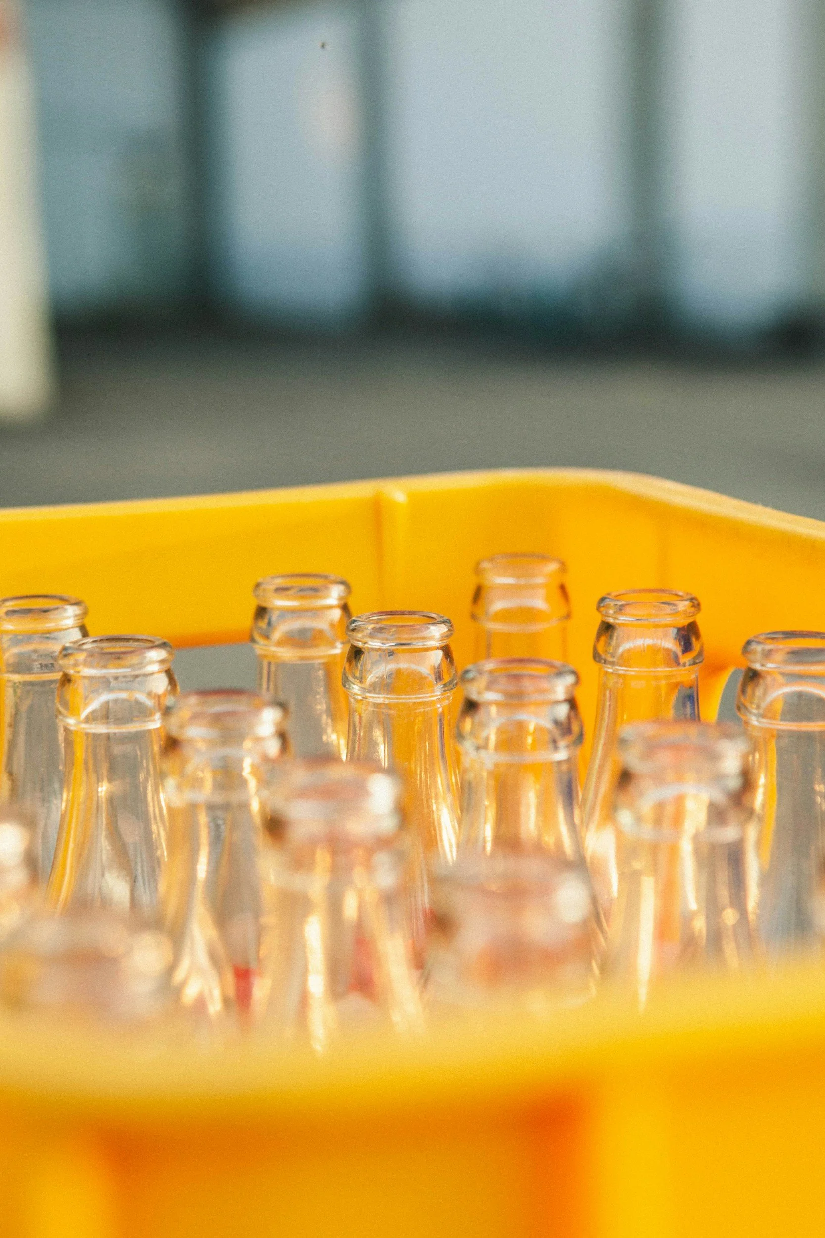 Several empty glass bottles placed in a yellow plastic tray, with a blurry background.