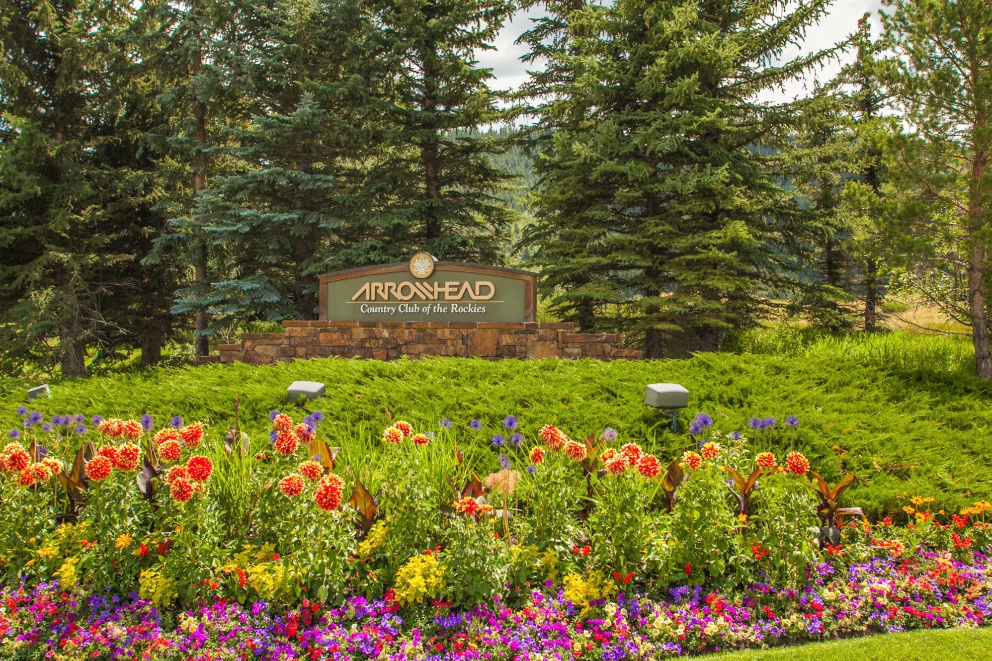 Entrance sign for Arrowhead Country Club of the Rockies surrounded by colorful flowers and green trees represented by Danielle Huidekoper, LIV Sotheby's International Realty.