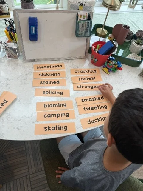 Child organizing paper cutouts with words related to different vocabulary categories on a desk inside a home office space.