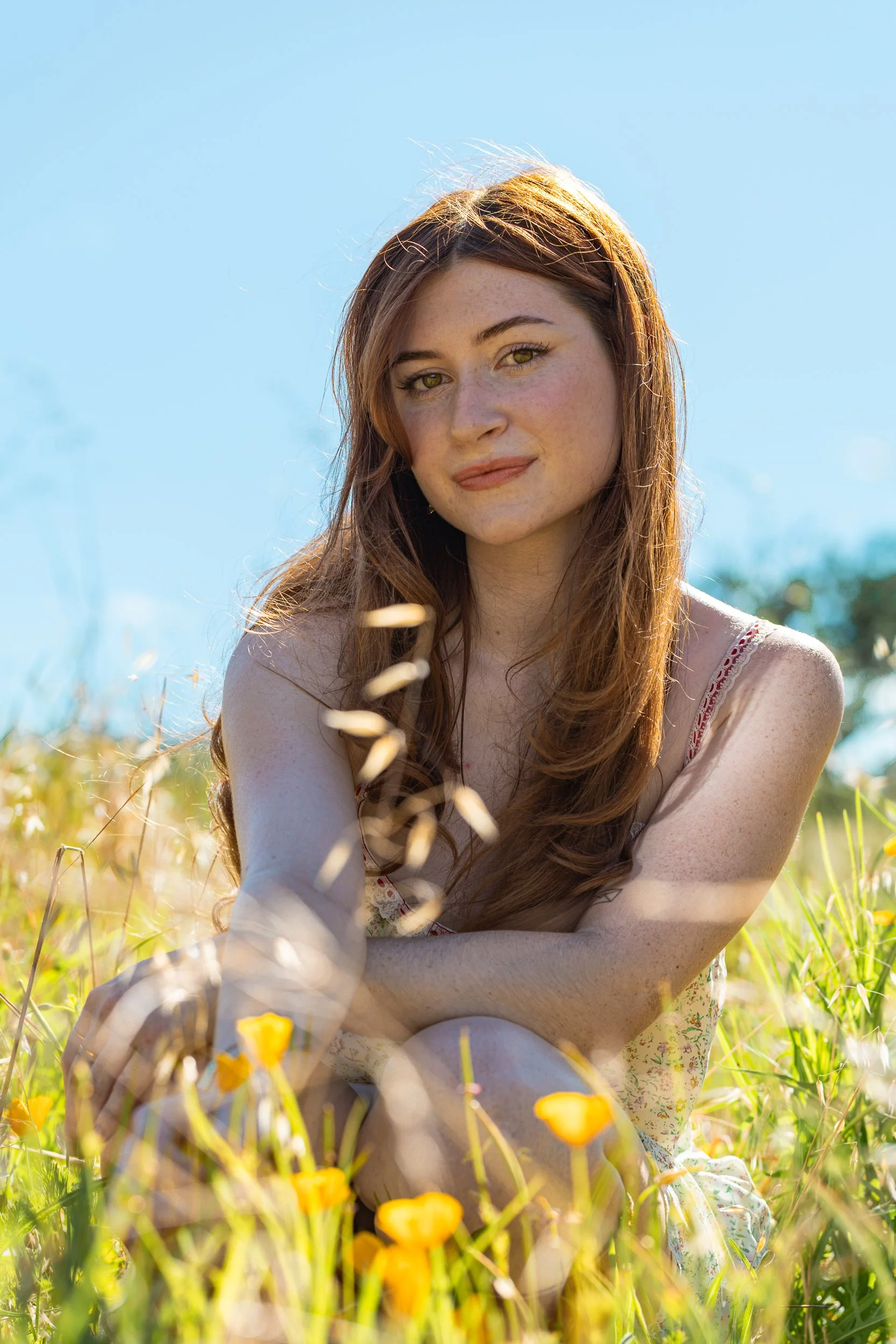 Young woman with long brown hair sitting in a meadow of yellow poppies under a bright blue sky