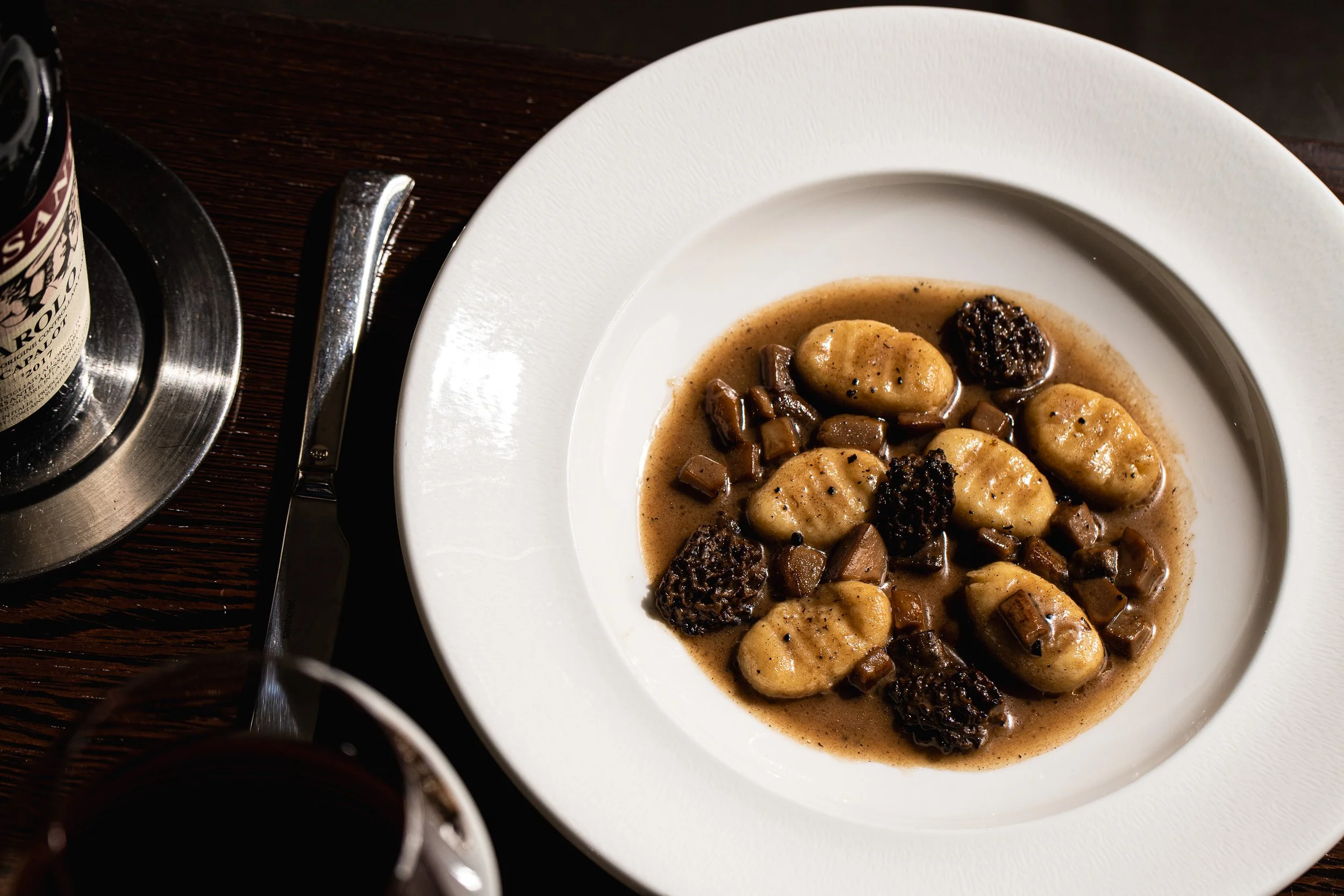 Gnocchi with morel mushrooms in a brown sauce in a white bowl at La Toque in Napa, with a glass of red wine nearby