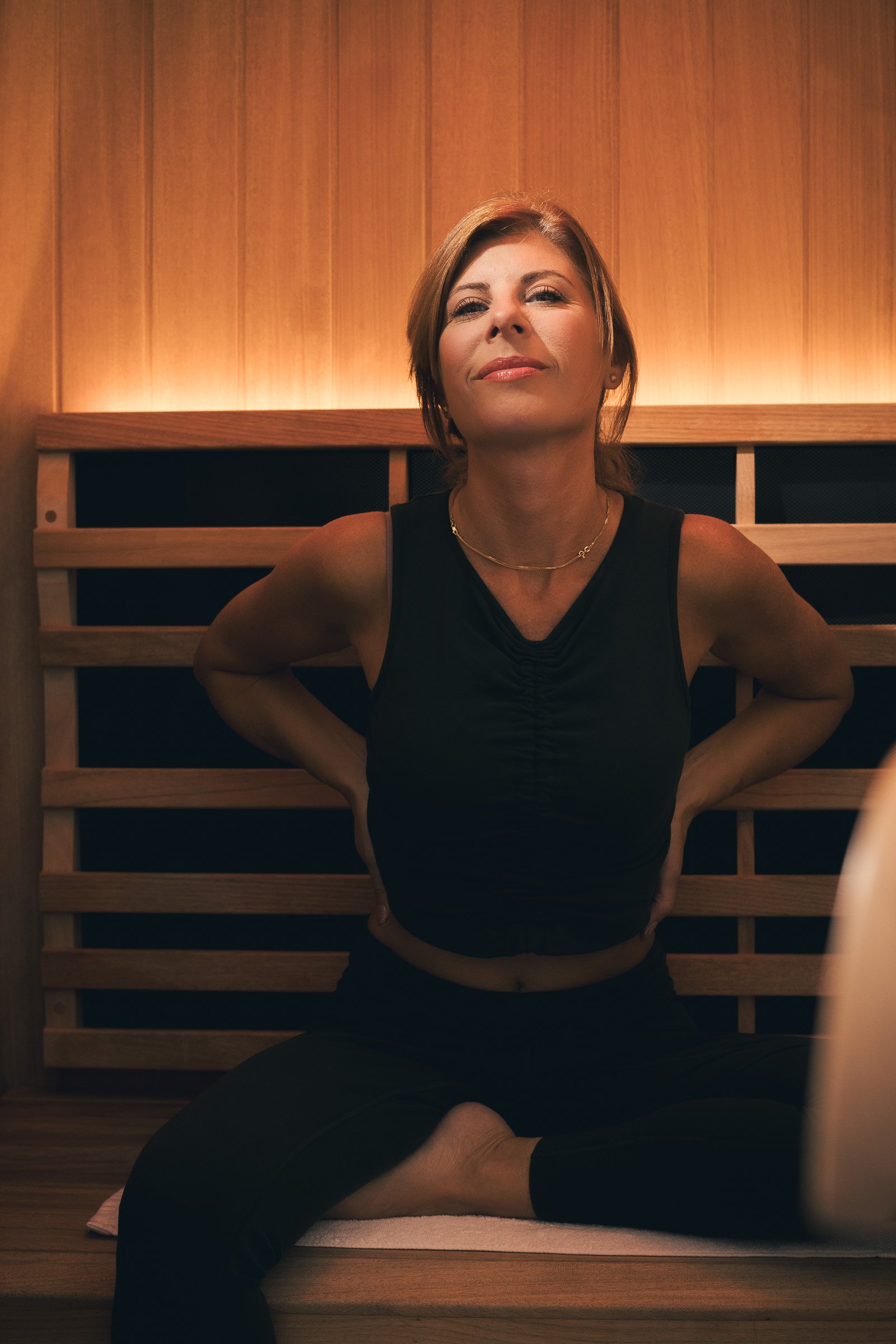 Woman in a dark top seated in a wood paneled sauna with warm backlight