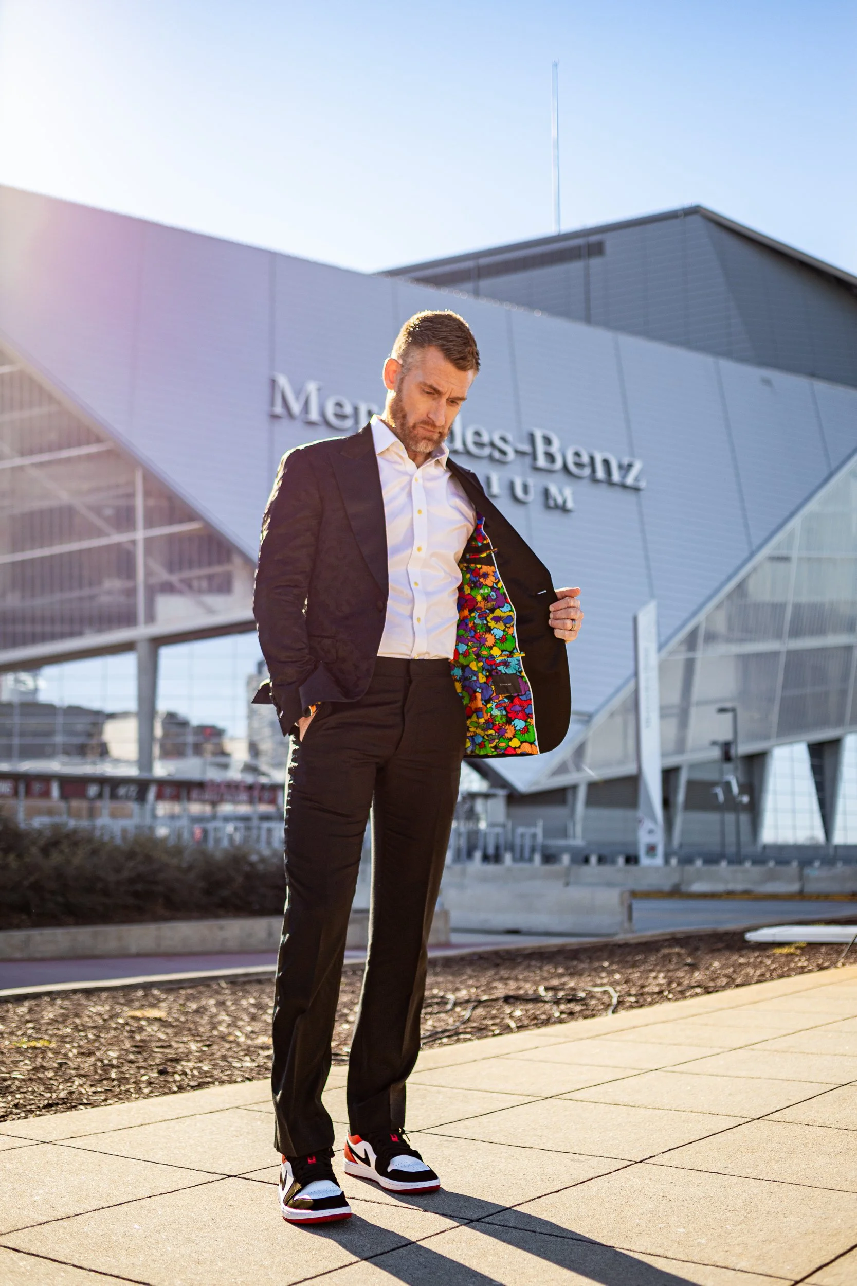 Man in a black suit with a colorful patterned lining standing with his jacket open outside Mercedes-Benz Stadium