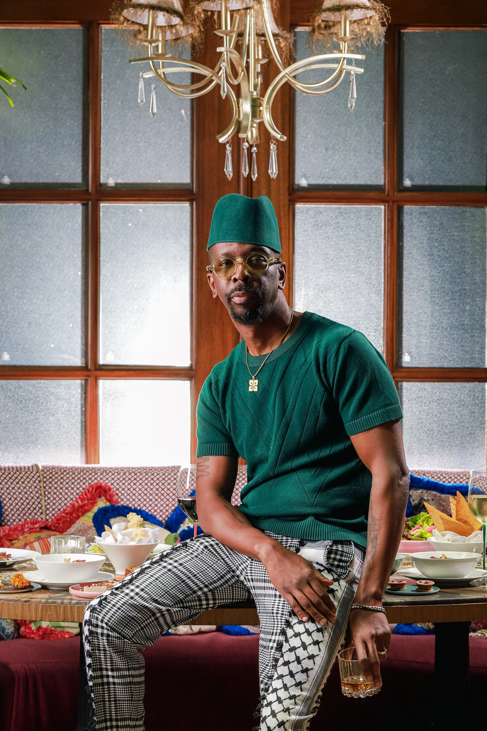 Man in a green tee and plaid pants seated at a table full of shared dishes