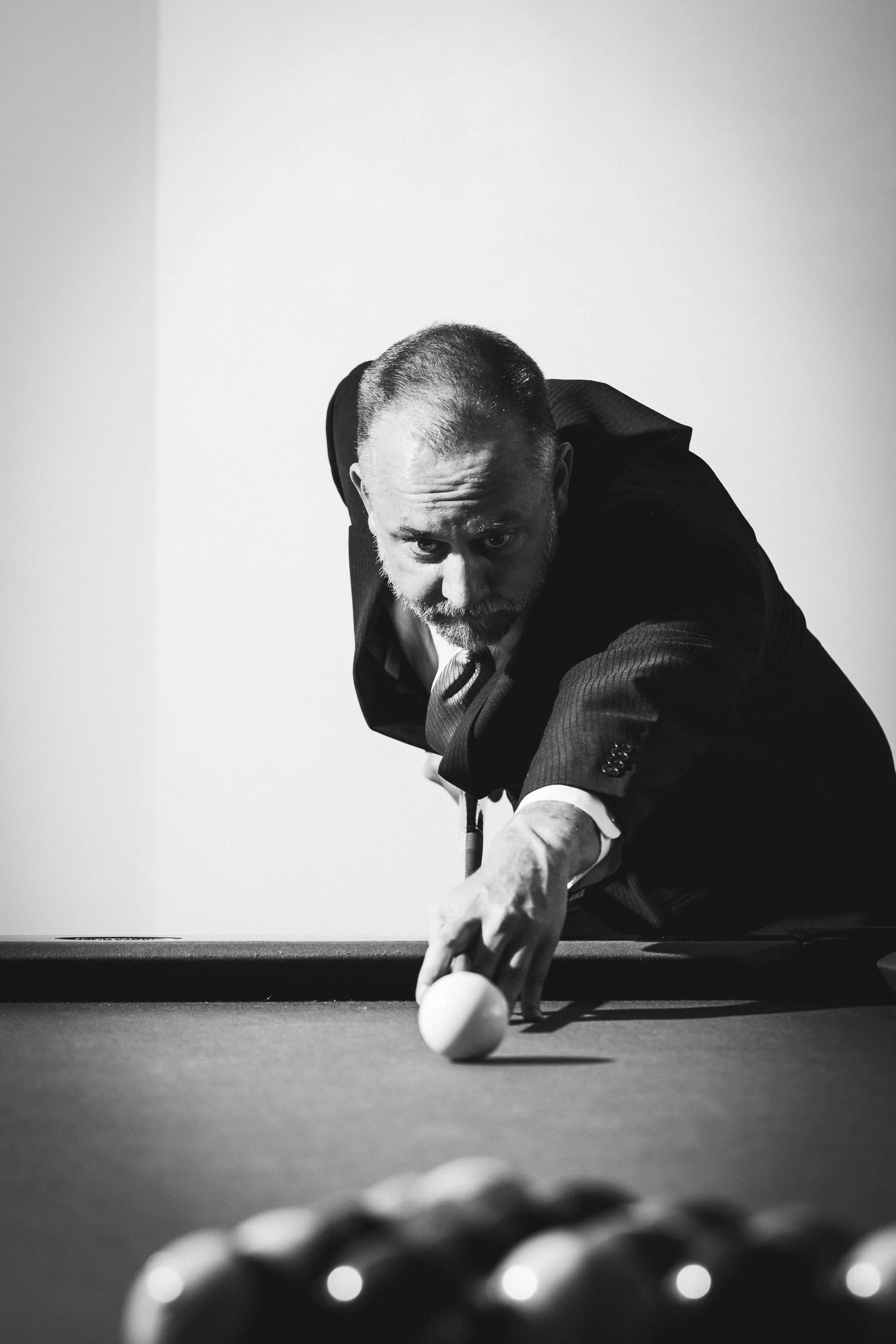 Black and white photo of a man in a dark suit leaning over a pool table lining up a shot