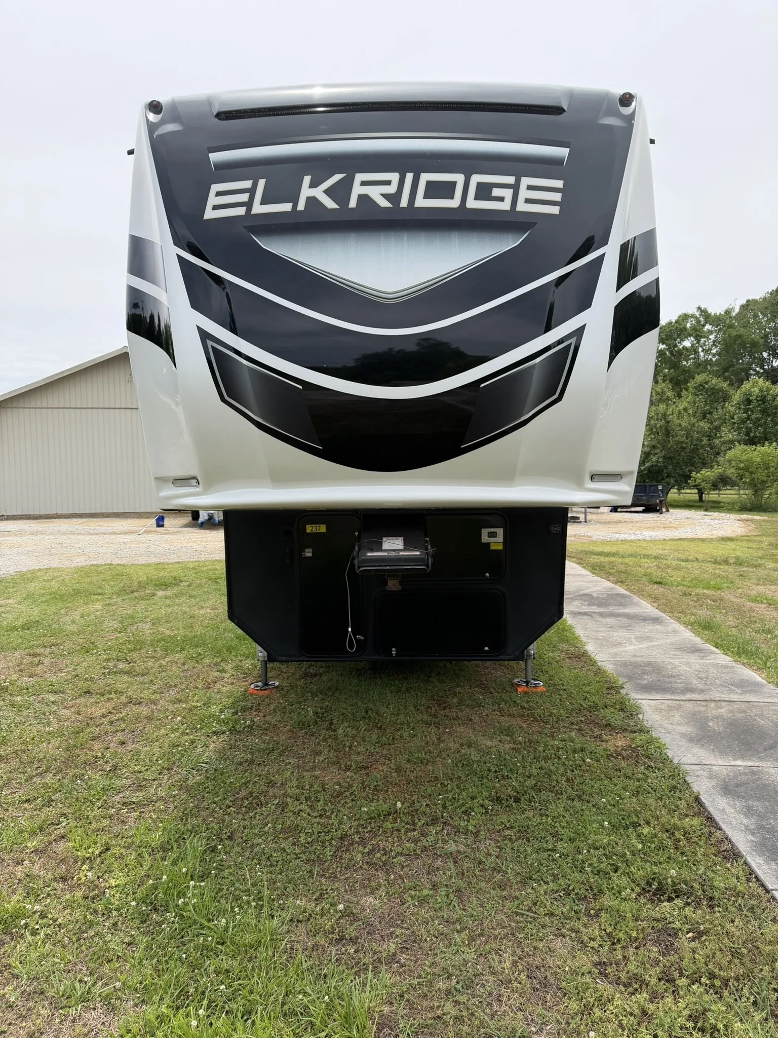 Front view of an Elkridge recreational vehicle or camper trailer parked on grass with trees and a building in the background.