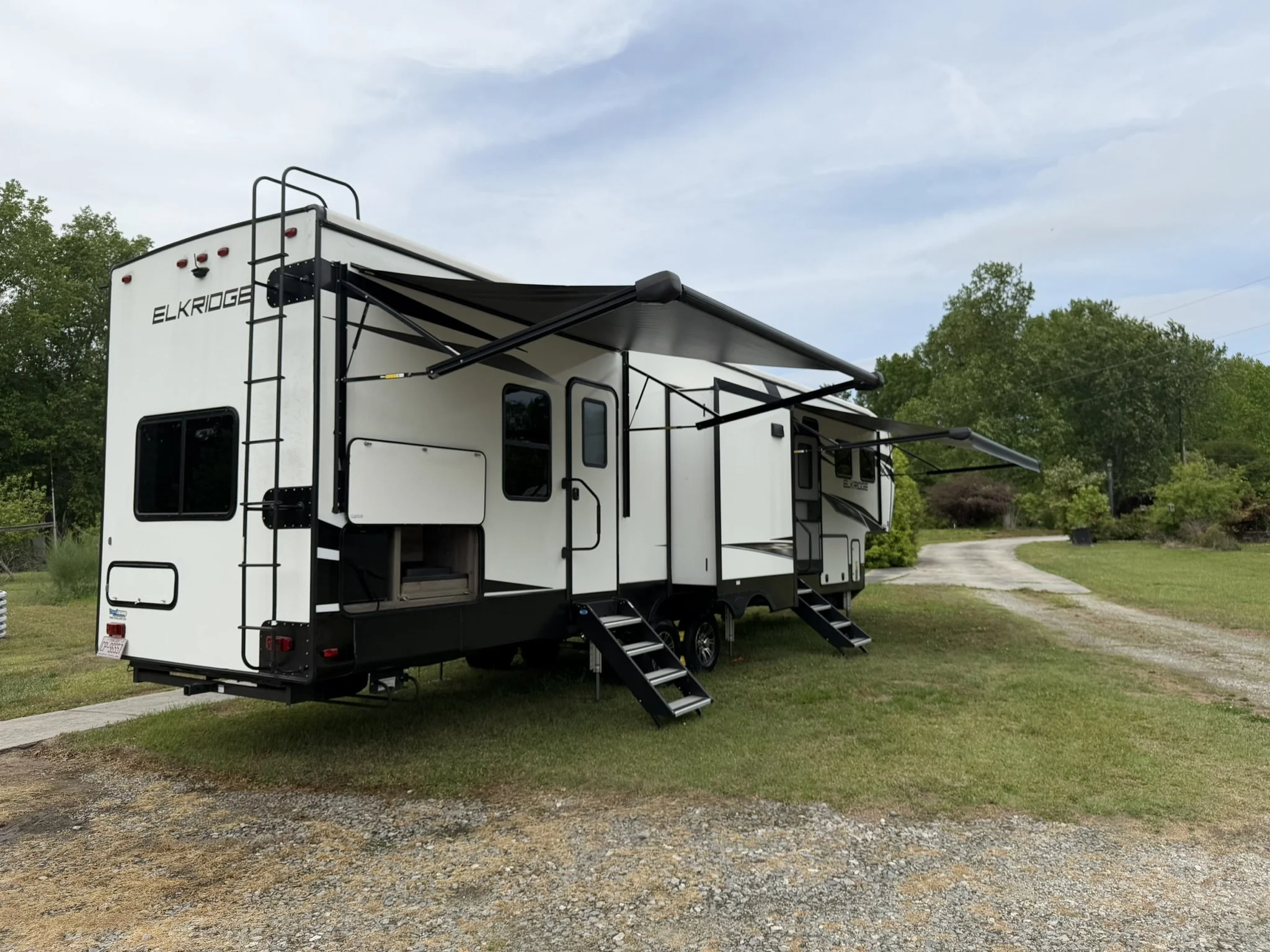 White ElkRidge RV with black accents parked on grass with trees and a cloudy sky in the background.