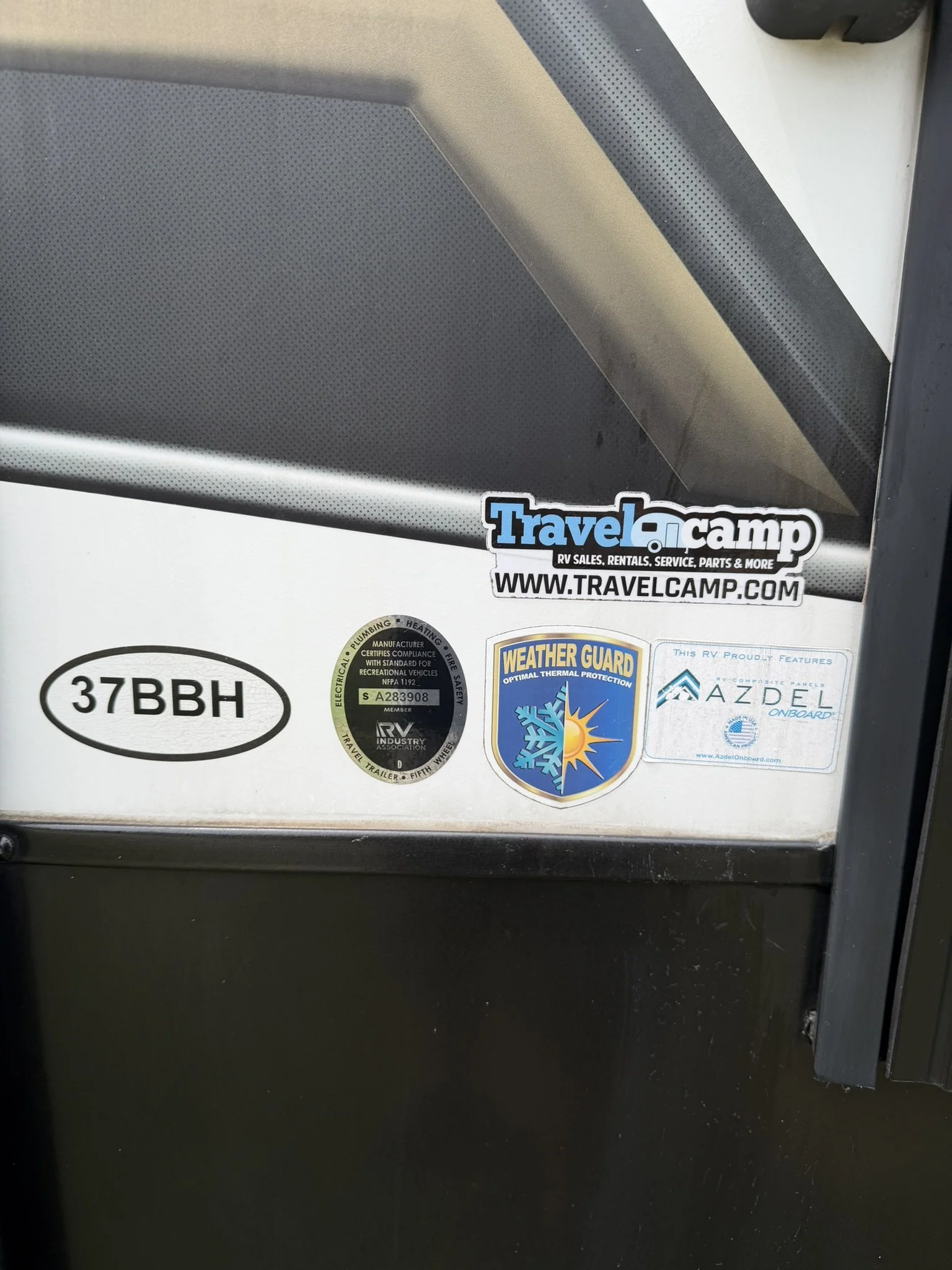 Close-up of a section of an RV with various stickers, including a website address, weather guard label, and a sticker with the code 37BBH.