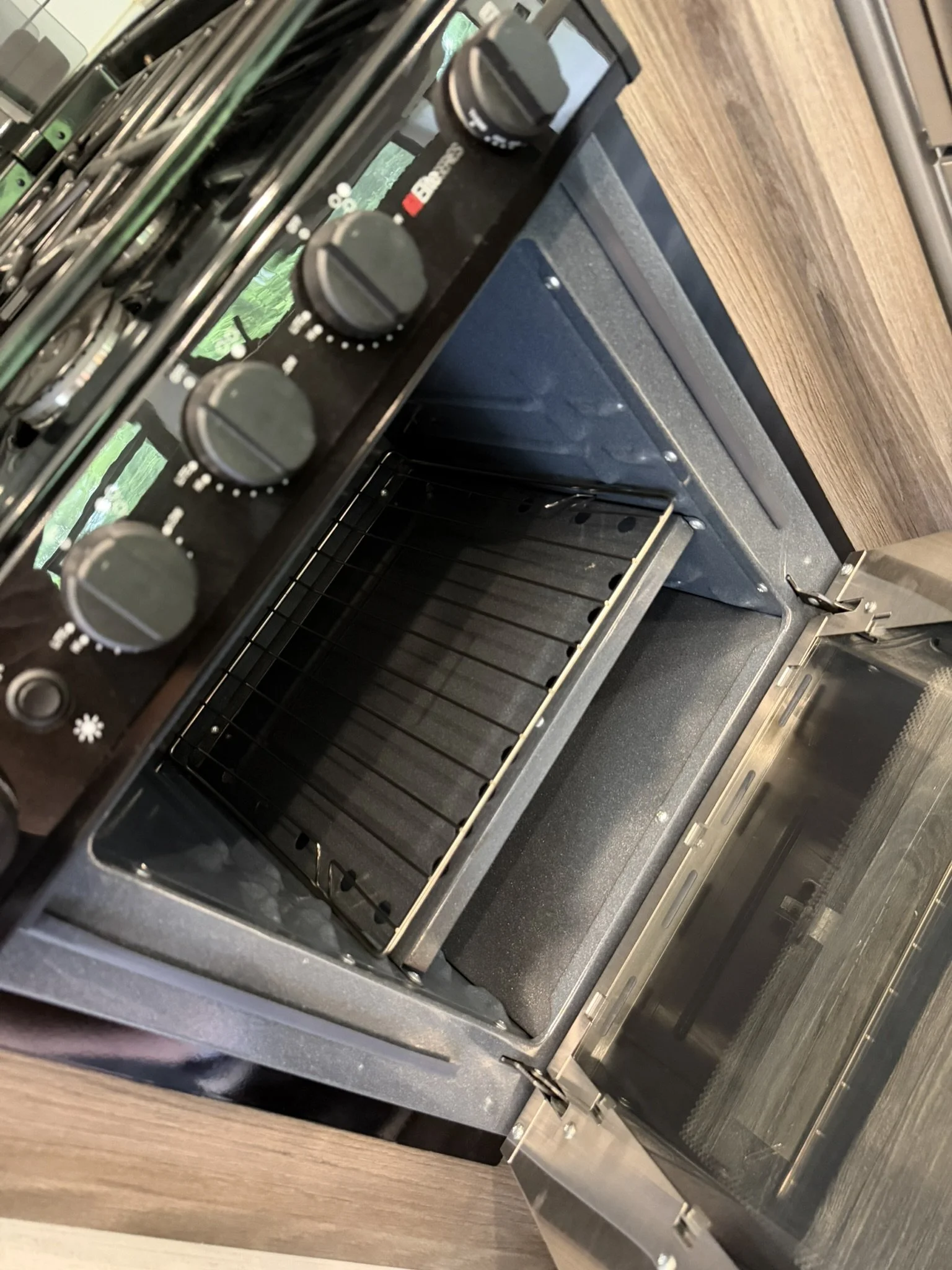 Empty stainless steel oven with the door open, showing oven racks inside, on a wooden countertop.