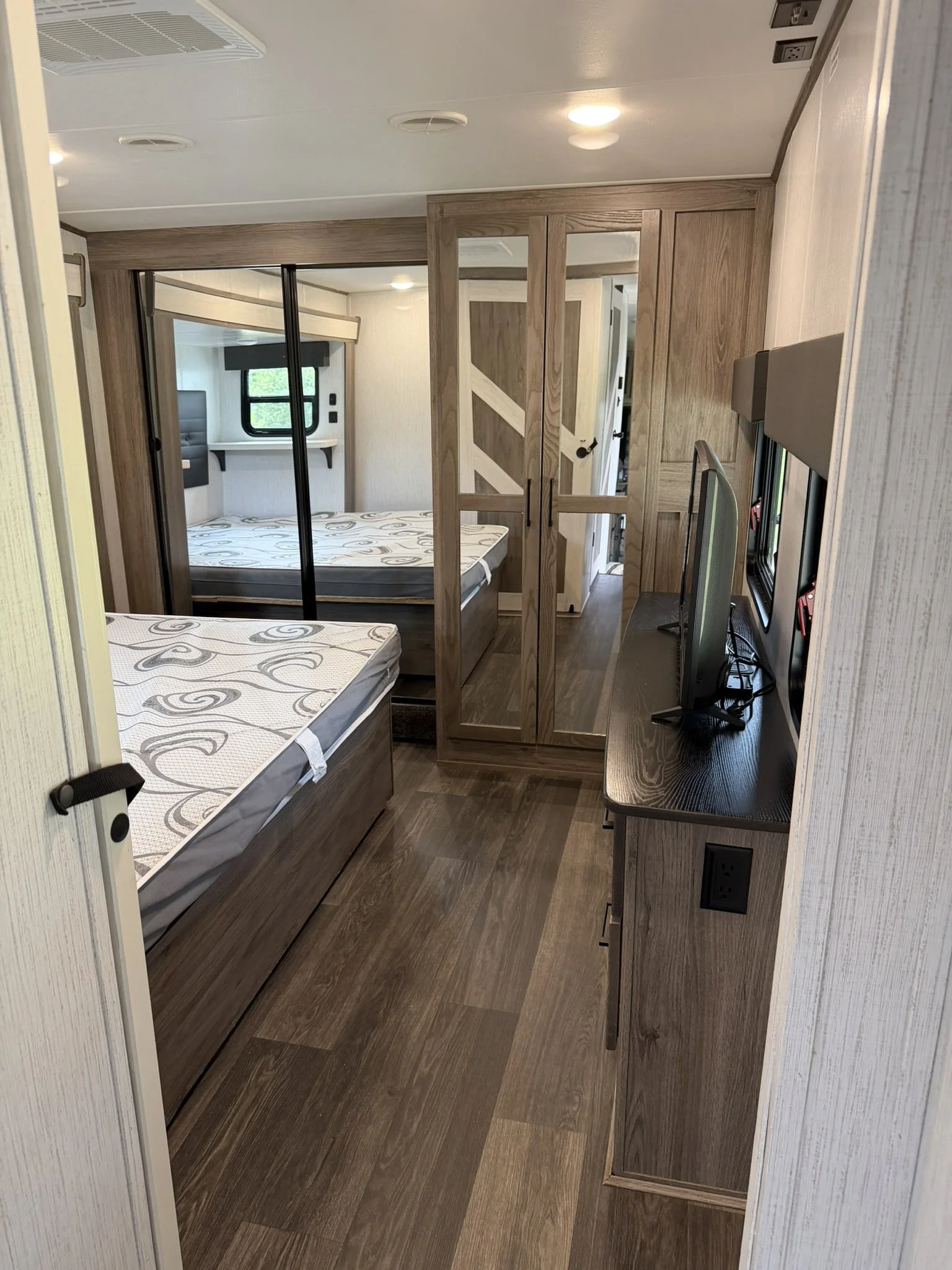 Interior of a camper or RV with two beds, a TV, and wooden cabinets.