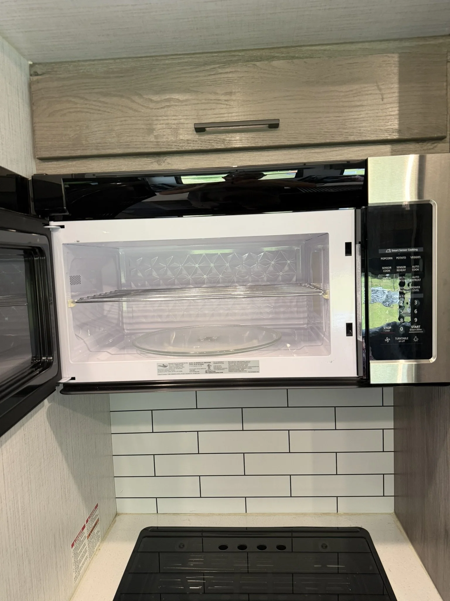 Open microwave oven on a kitchen counter with heating glass plate inside, against tiled backsplash and wooden cabinets.