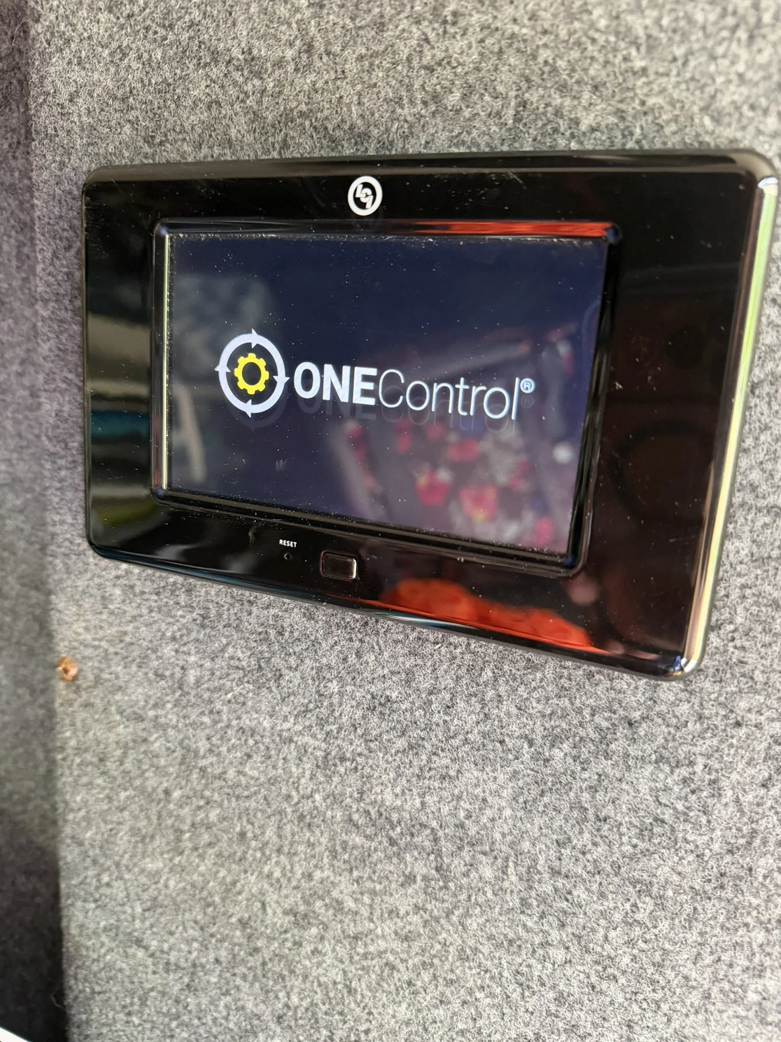 A black device with the text 'ONE Control' displayed on its screen, lying on a gray fabric surface.