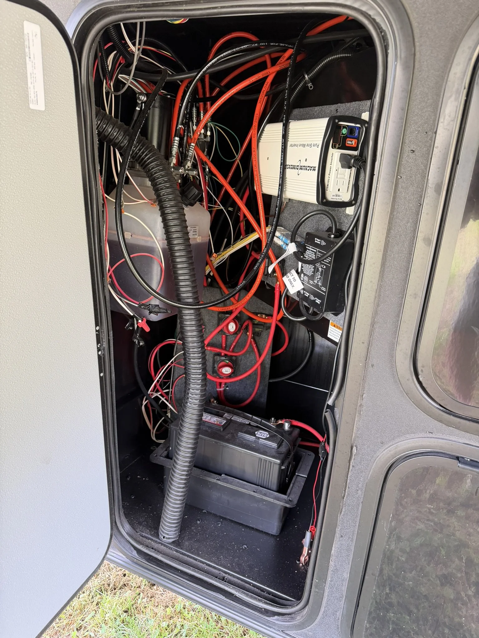 Inside an industrial or RV electrical compartment showing a battery, wiring, and electrical devices.