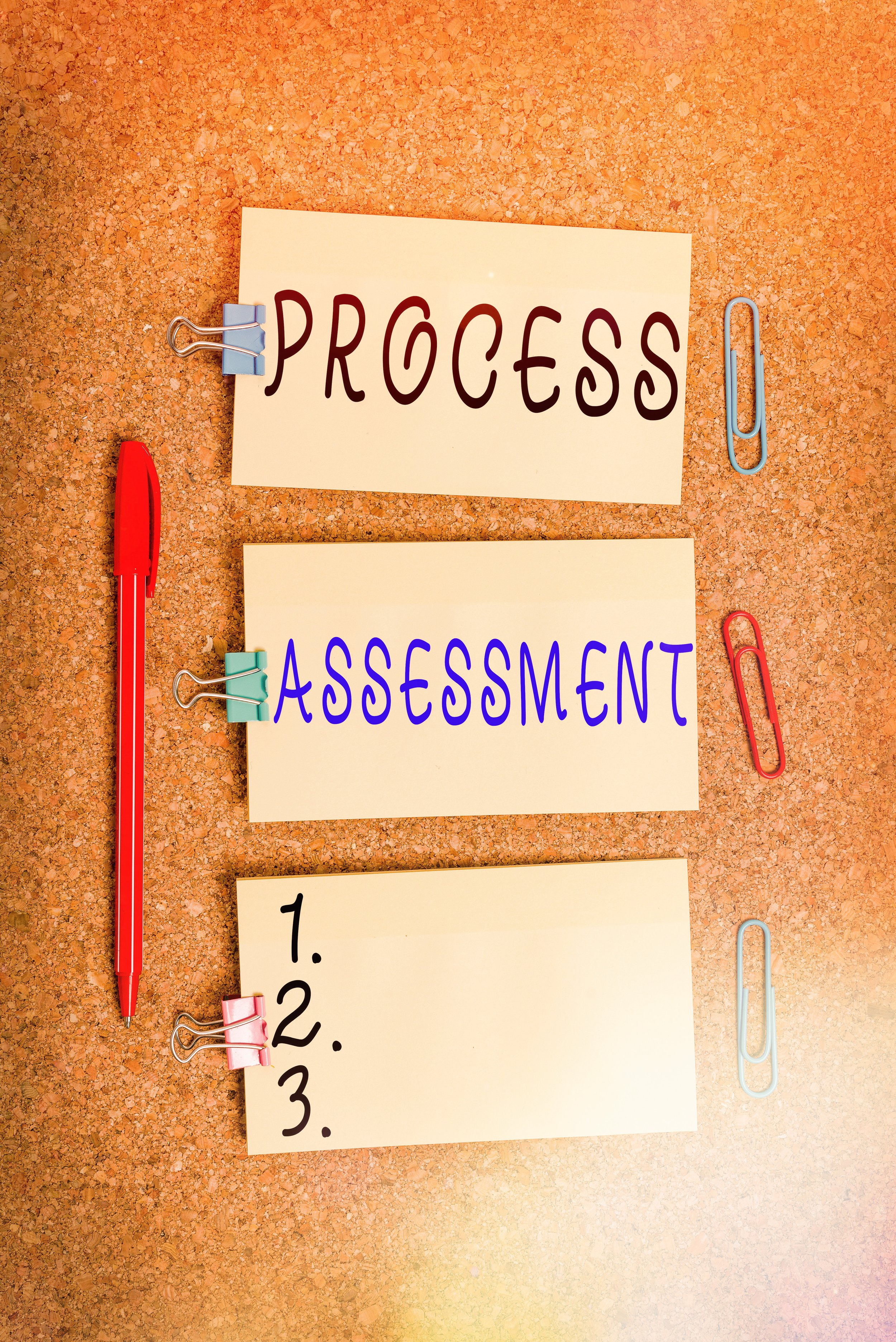 cork board with a red pen, 3 notes : 1 - Process, 2 - Assessment, 3 - 1.2.3. and several paperclips