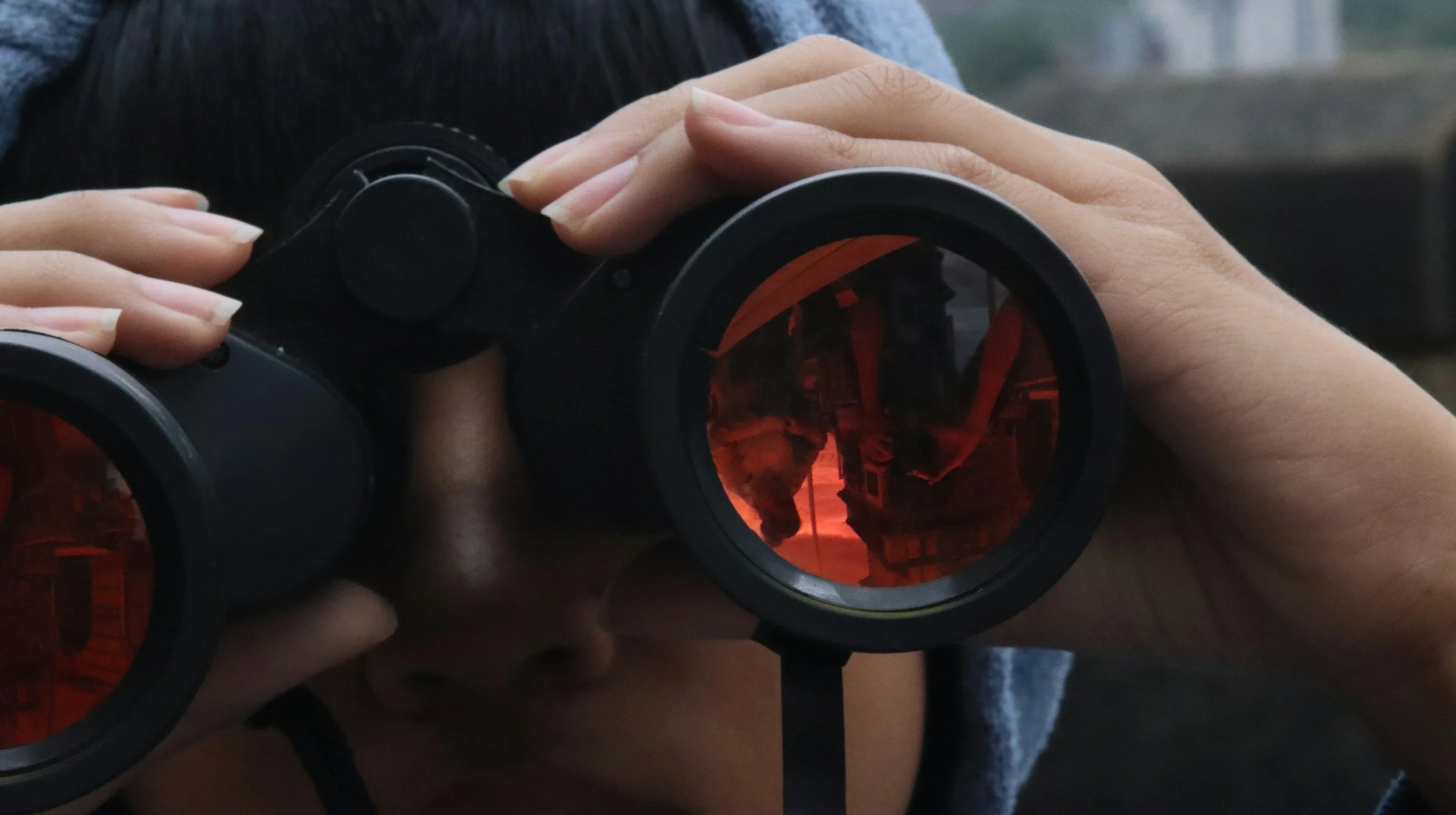 Close-up of a person holding binoculars with a red-tinted view.