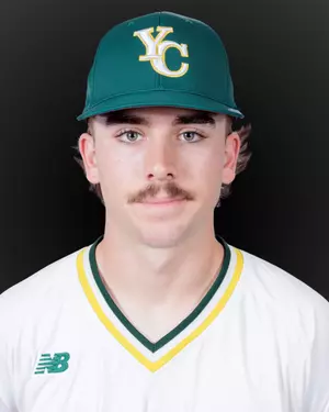 Portrait of a young man with a mustache wearing a green baseball cap with yellow and white 'YC' logo and a white sports jersey with green and yellow trim.