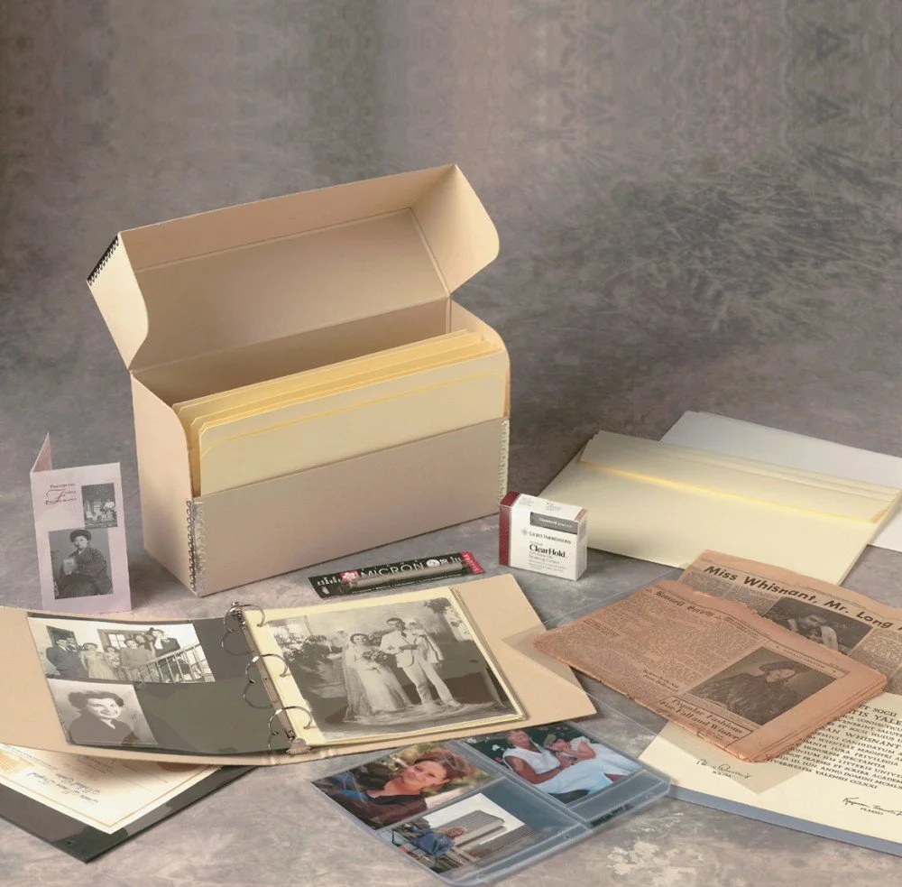 A collection of vintage photographs, newspaper clippings, and memorabilia, organized in albums and folders with a storage box in the background.