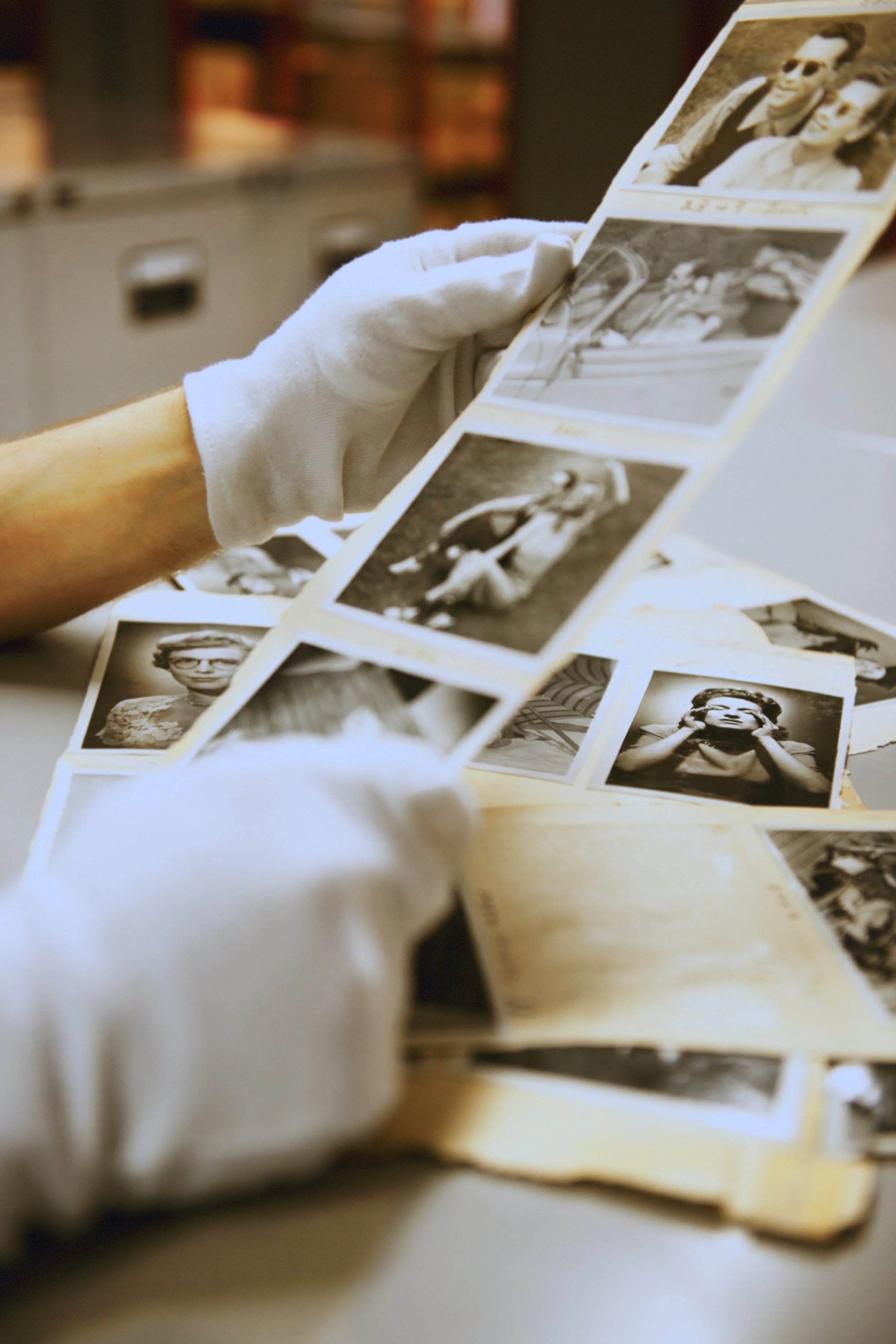 A person wearing white gloves holding a strip of black-and-white photographs.